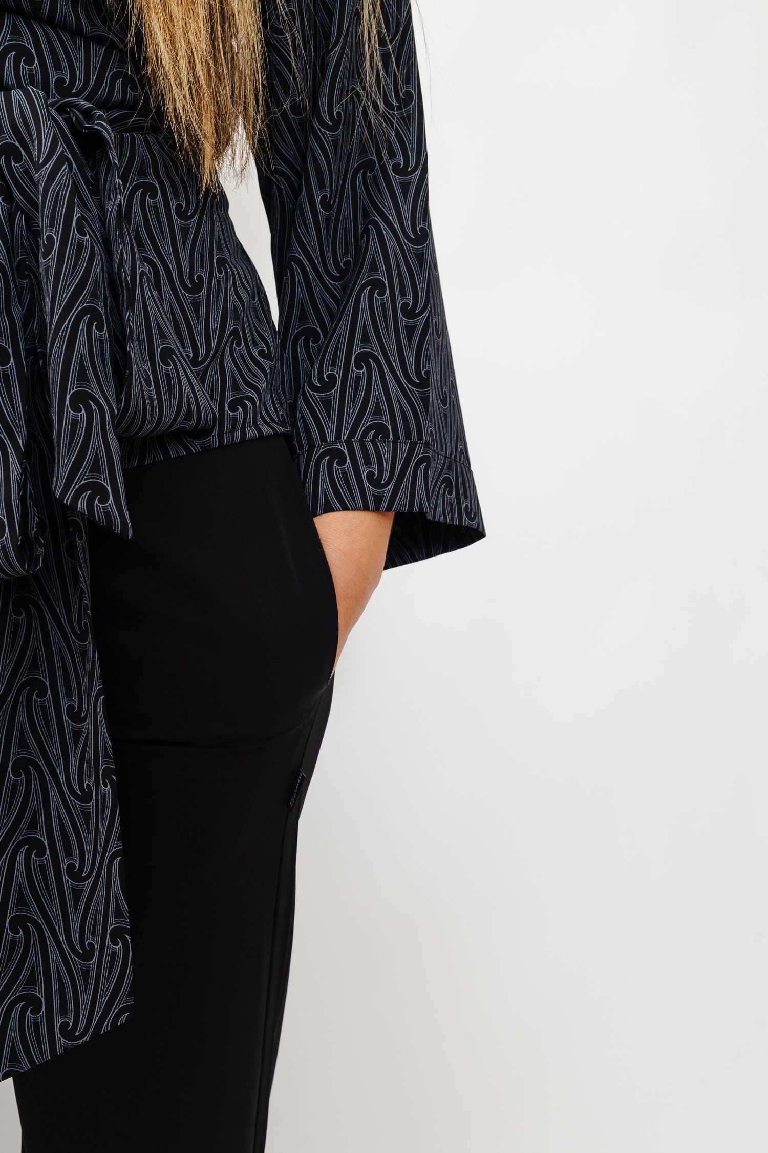A close-up view of a black patterned blazer with abstract swirl designs and a side pocket detail.