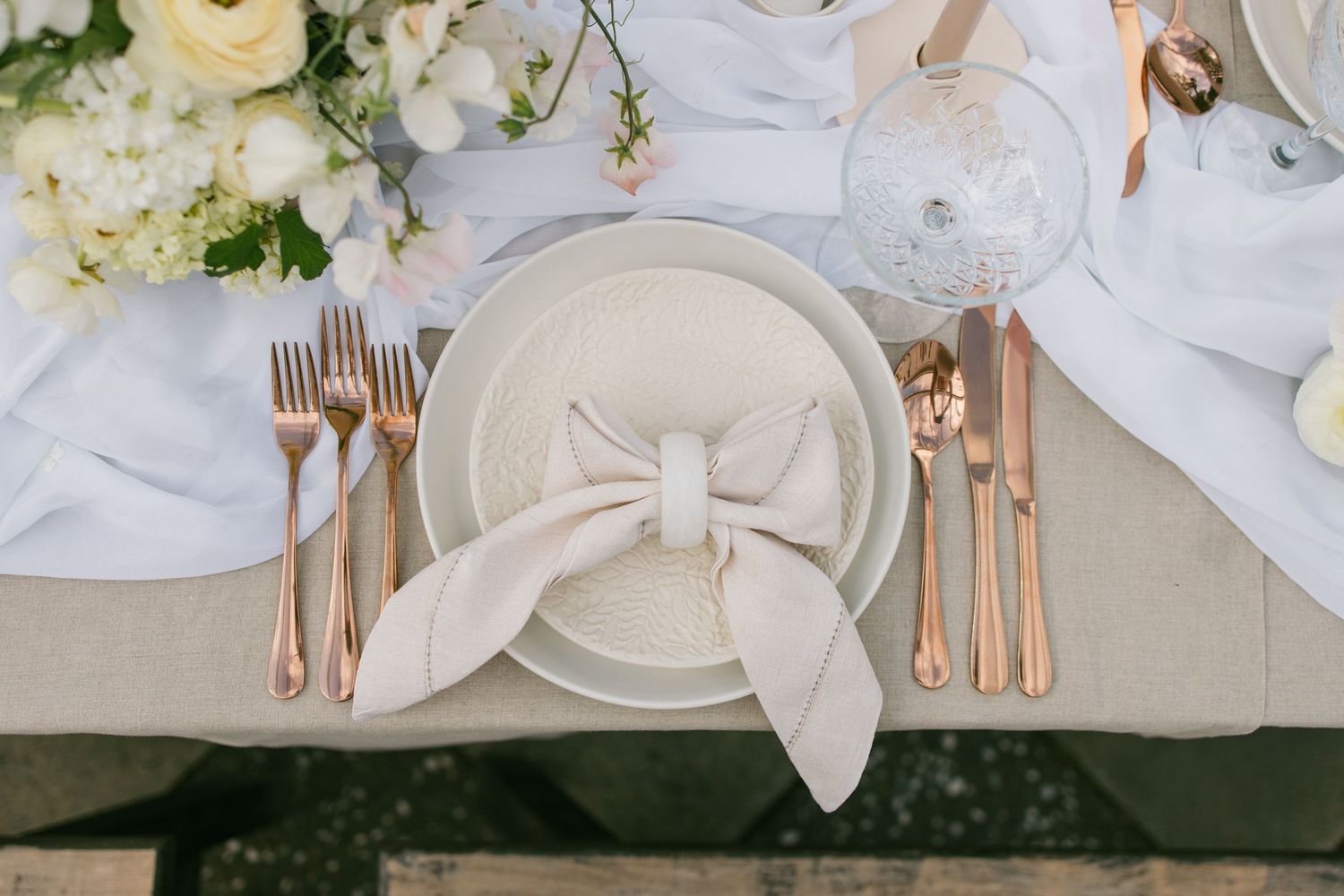White and cream wedding table settings with elegant floral centerpieces and rose gold flatware on neutral linens.