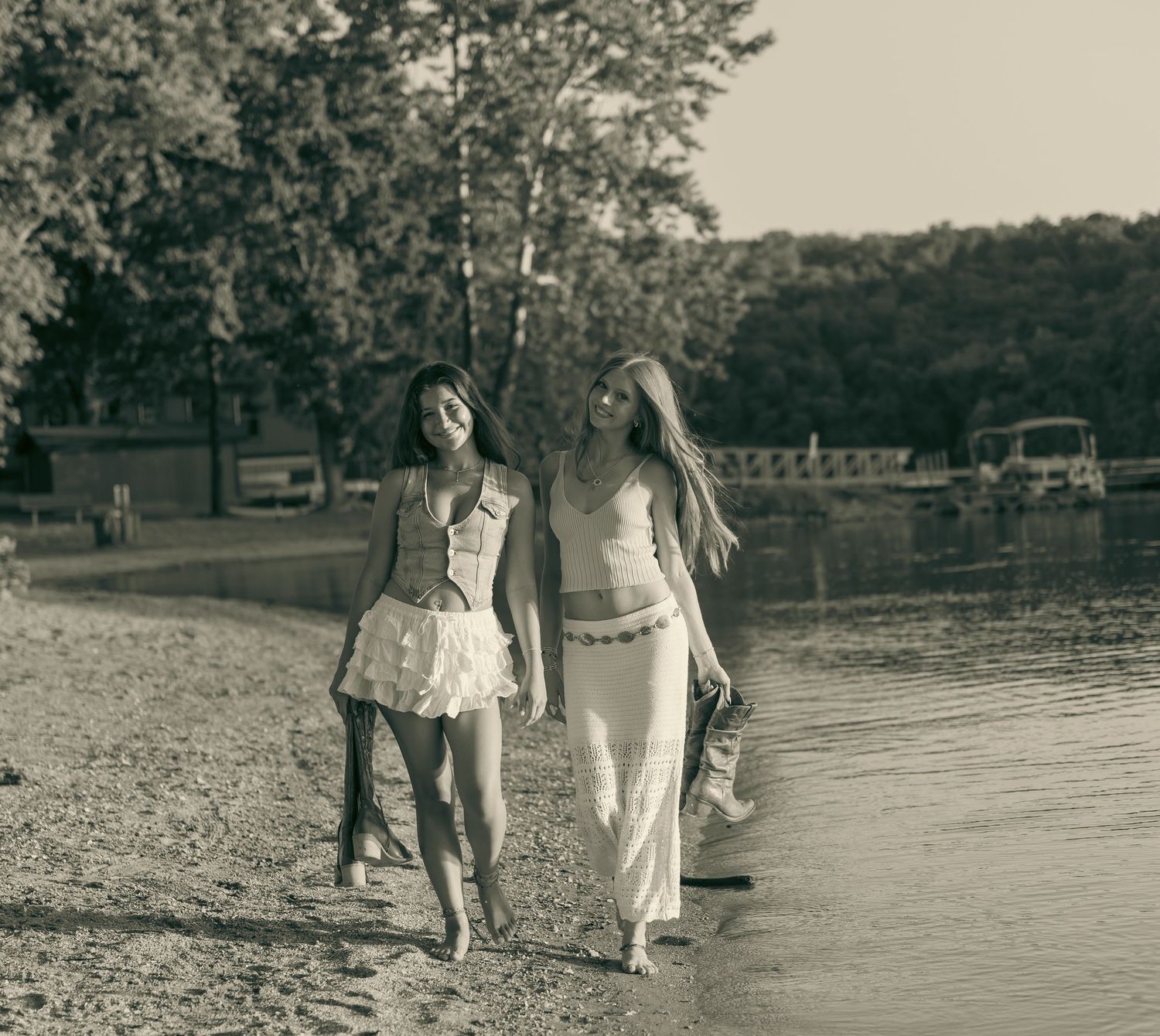 Two women walking barefoot along a sandy beach shore in vintage sepia tone photography.