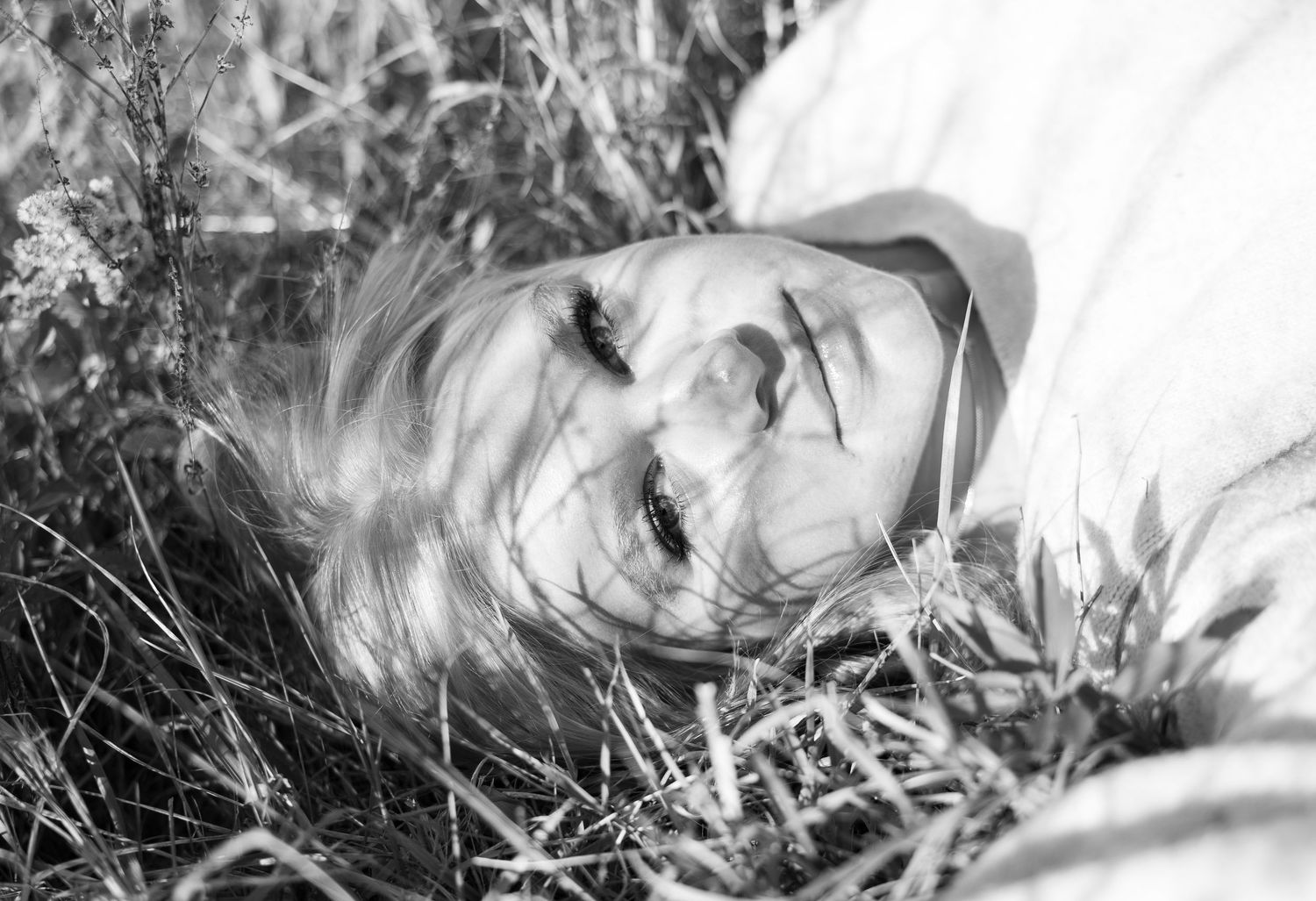 Black and white close-up of a smiling blonde senior lying peacefully in a field of grass and wildflowers.