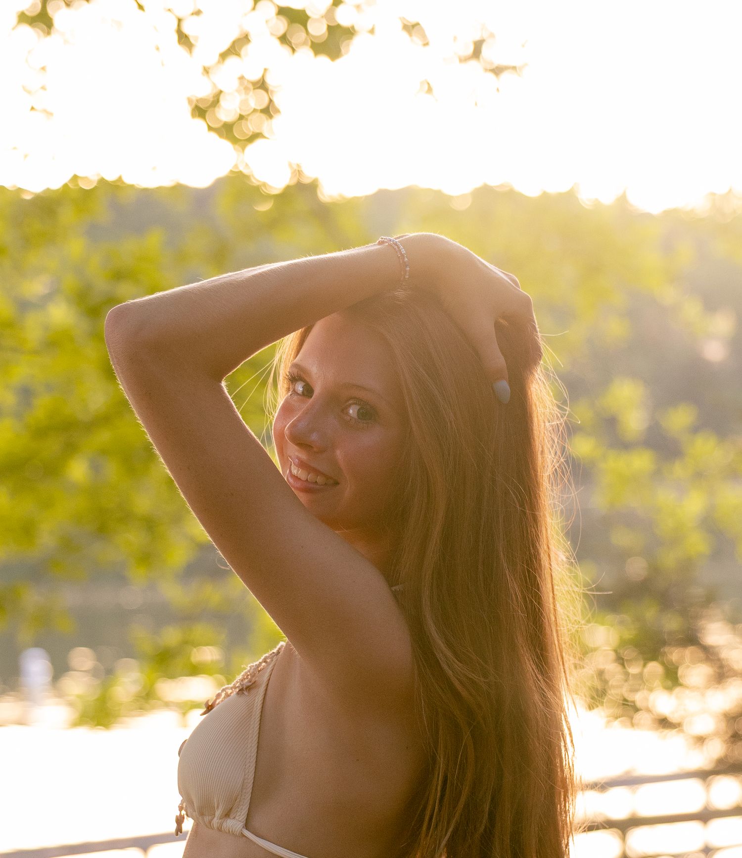 Beautiful young woman with long hair posing outdoors in warm golden sunset light.