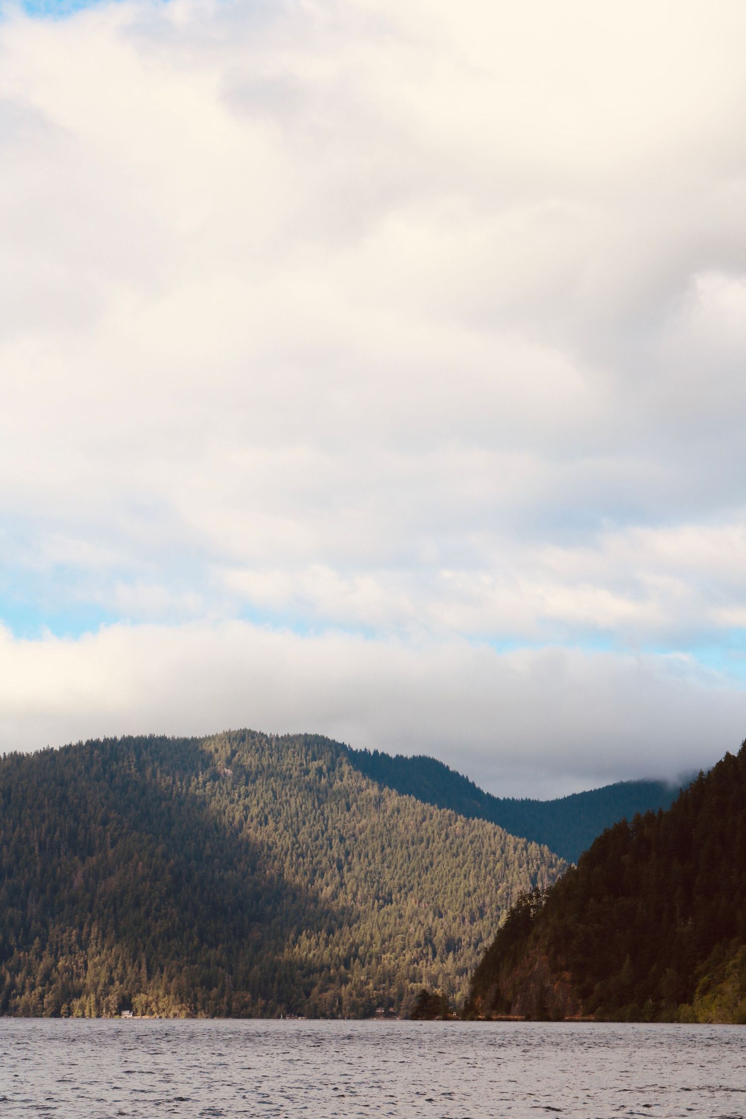 Forested mountain peaks rise above a serene lake under a partly cloudy sky in the Pacific Northwest.