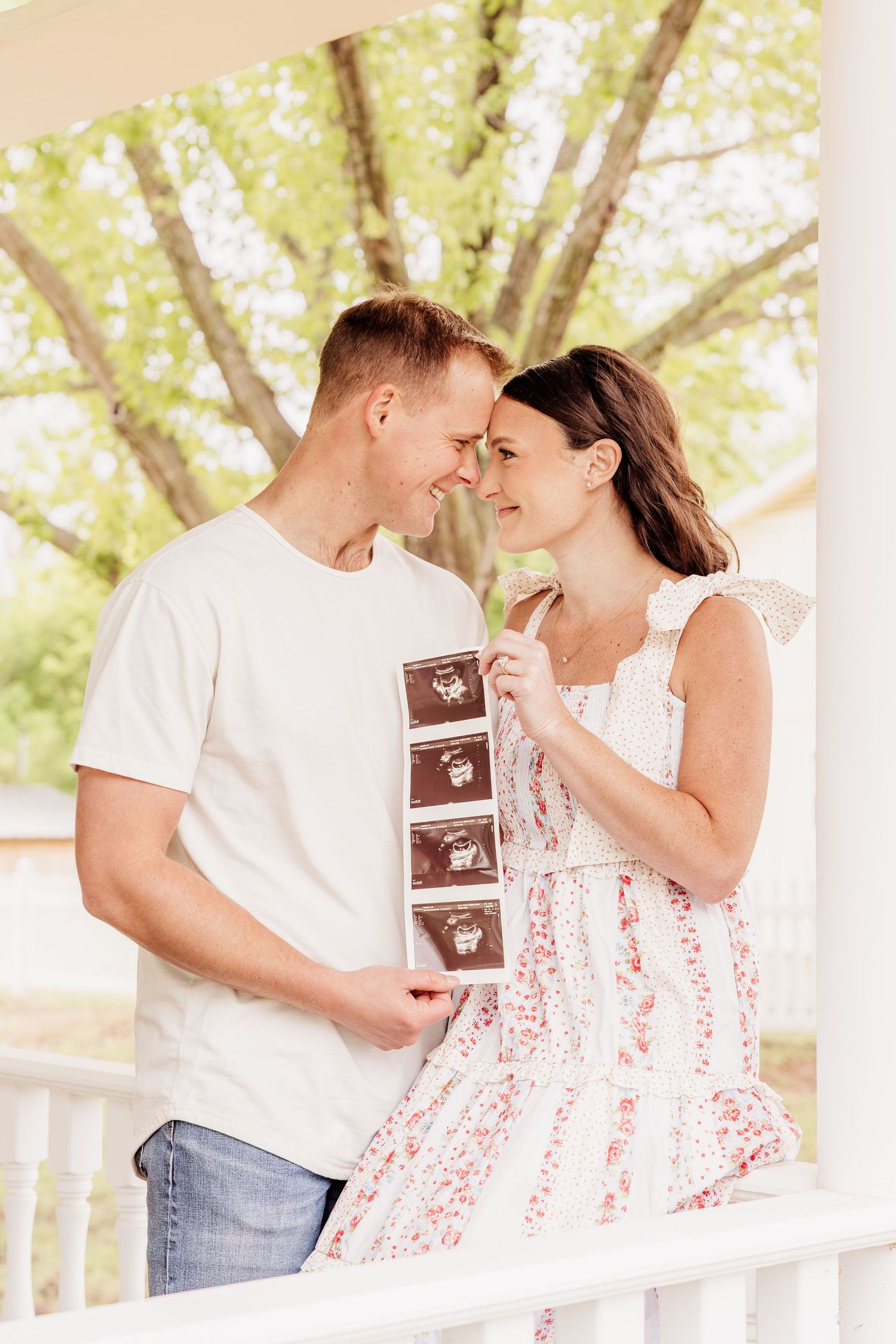 Happy couple holding ultrasound photos on a porch, sharing an intimate moment announcing their pregnancy.
