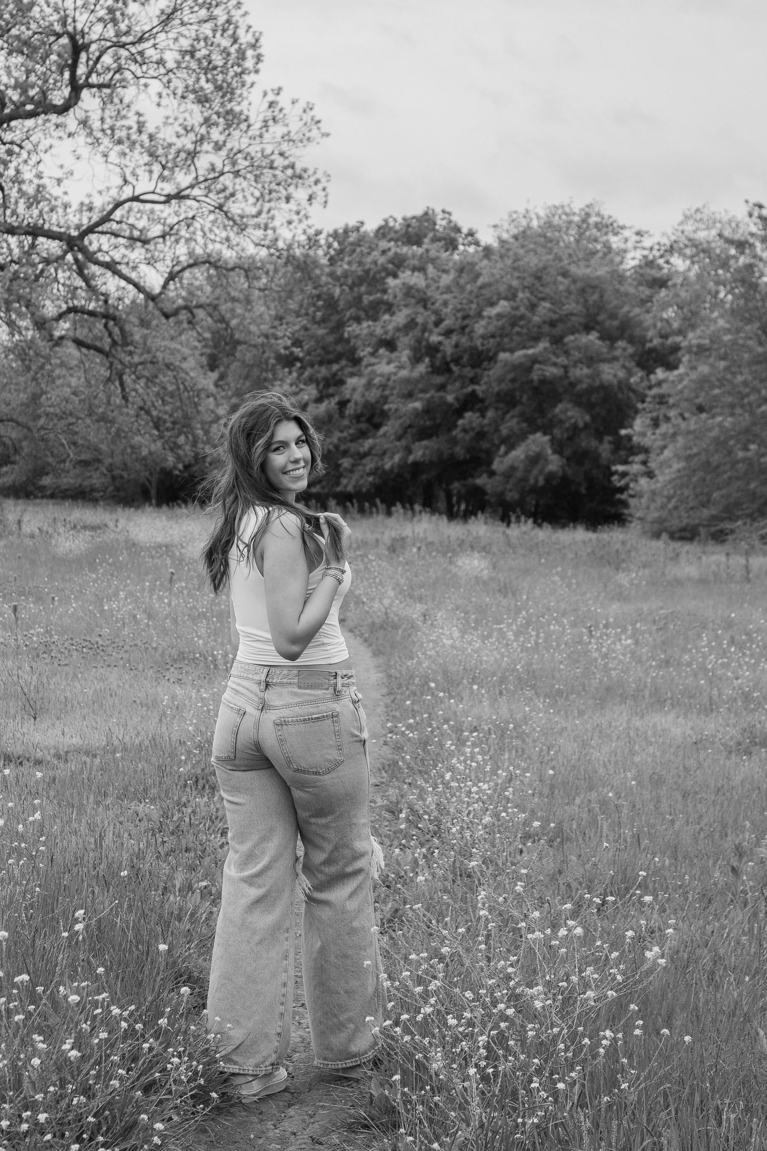 Person in light clothing stands in wildflower field during black and white outdoor photoshoot.
