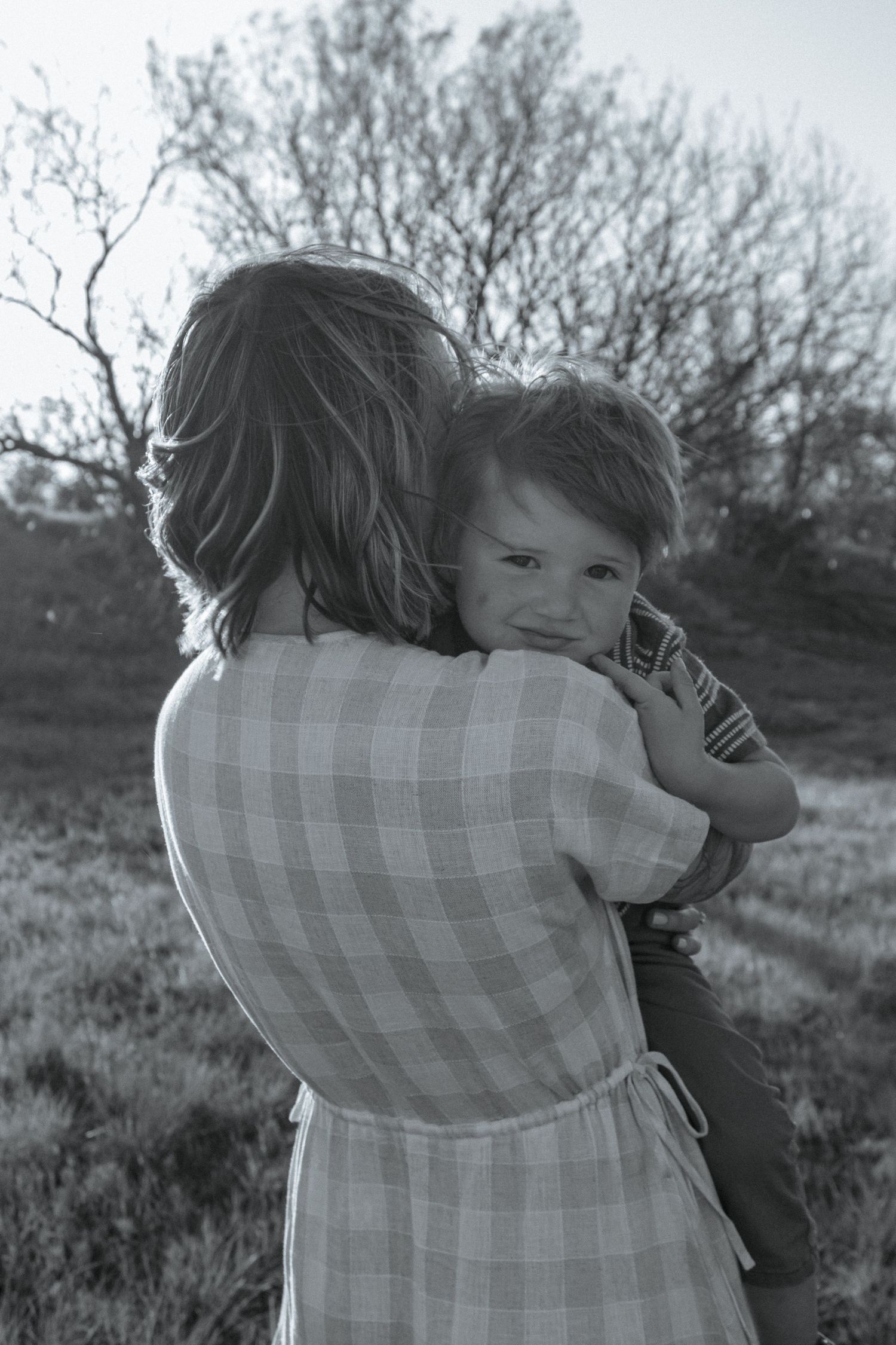 Black and white photo of parent holding child outdoors in a gingham dress.