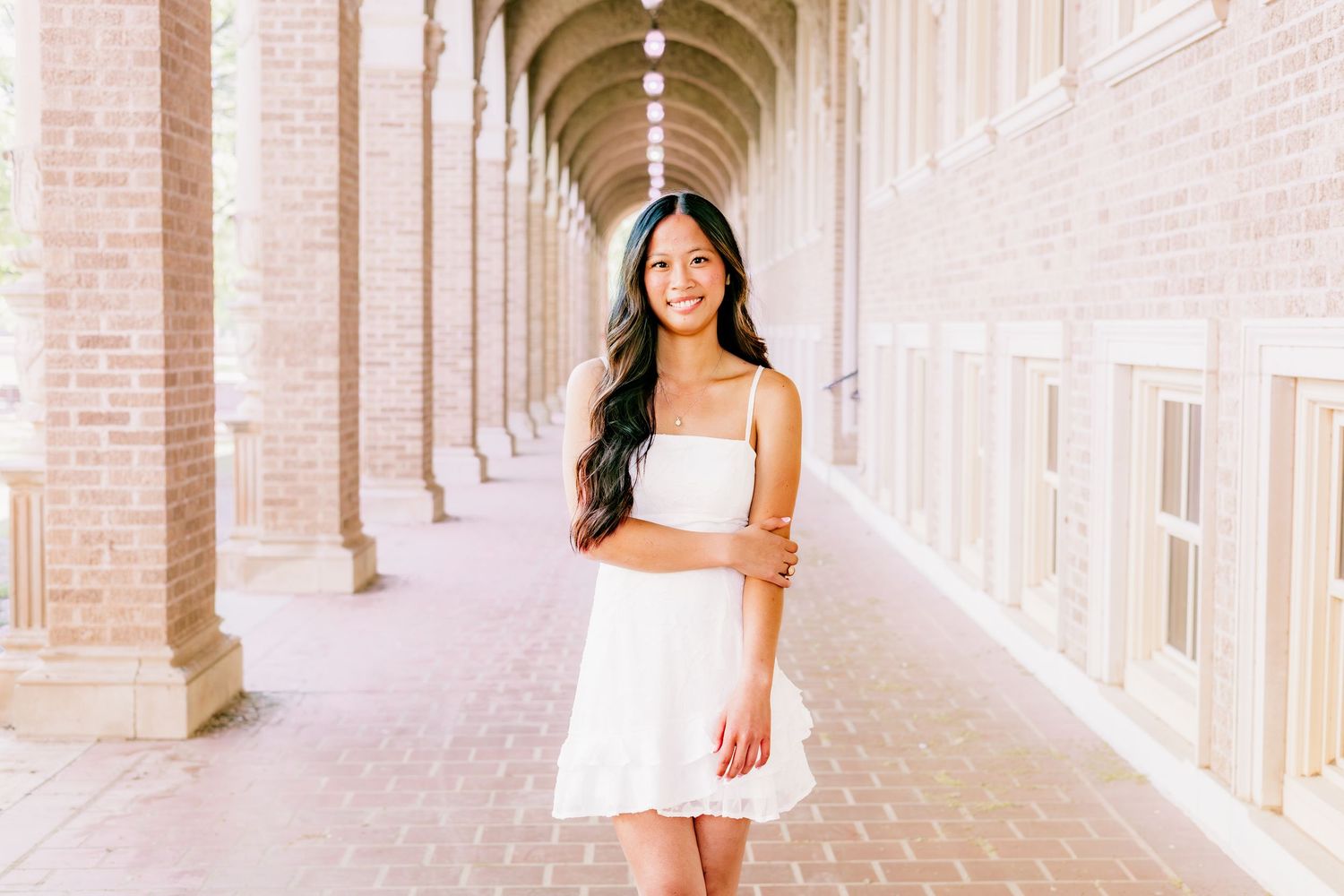 Young woman in white dress smiling in brick archway corridor, perfect for senior portrait photography.