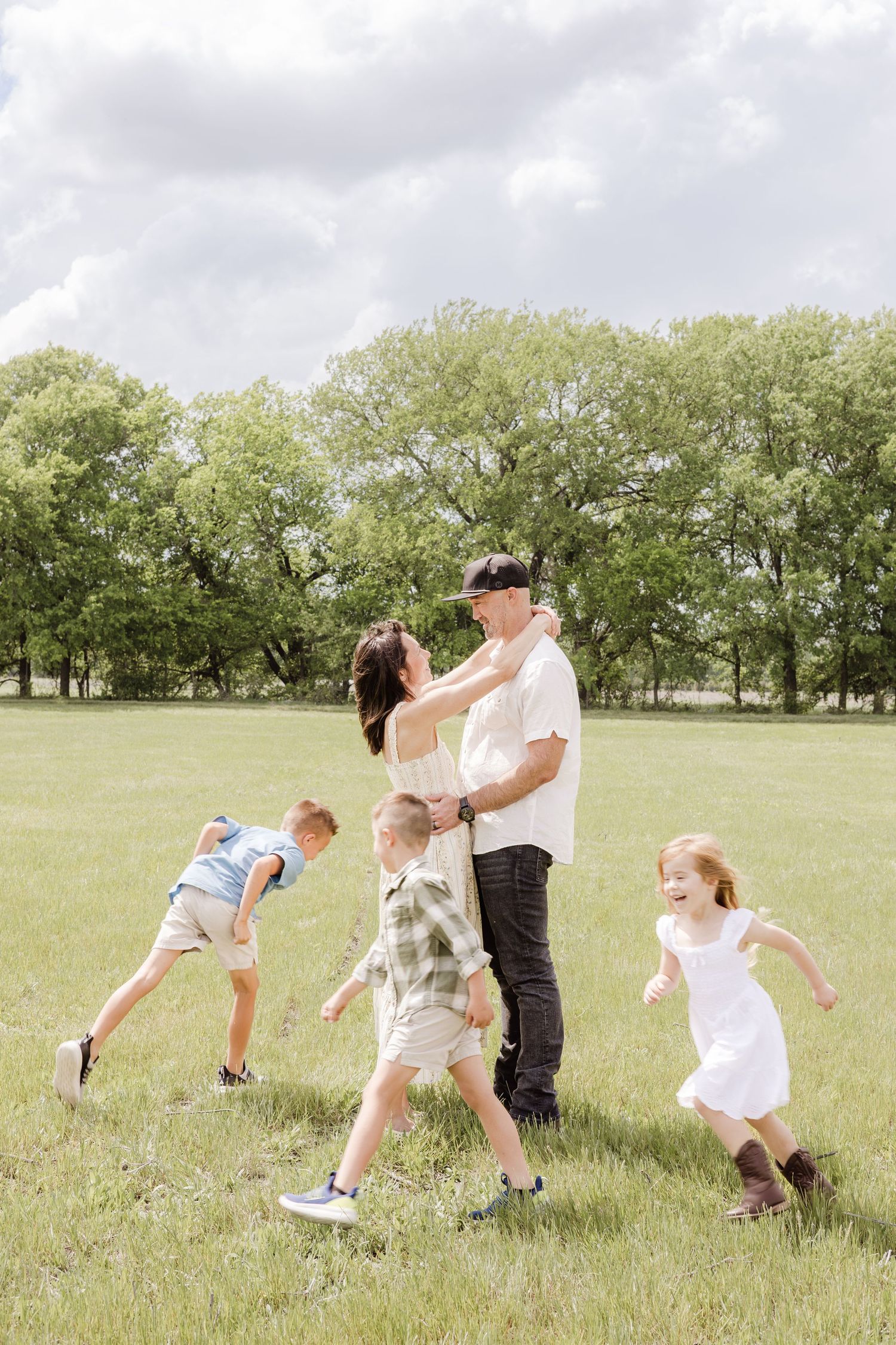 A joyful family with three children playing around their parents in a lush green park on a cloudy day.