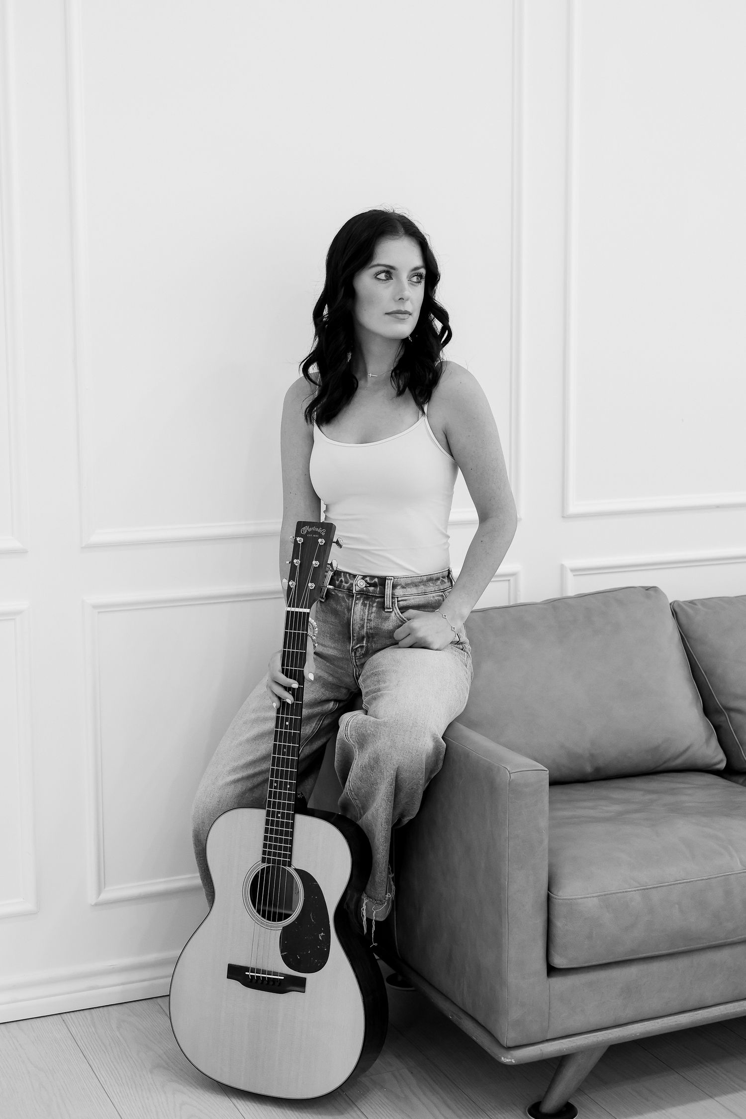 Black and white photos of person sitting with acoustic guitar on grey couch.