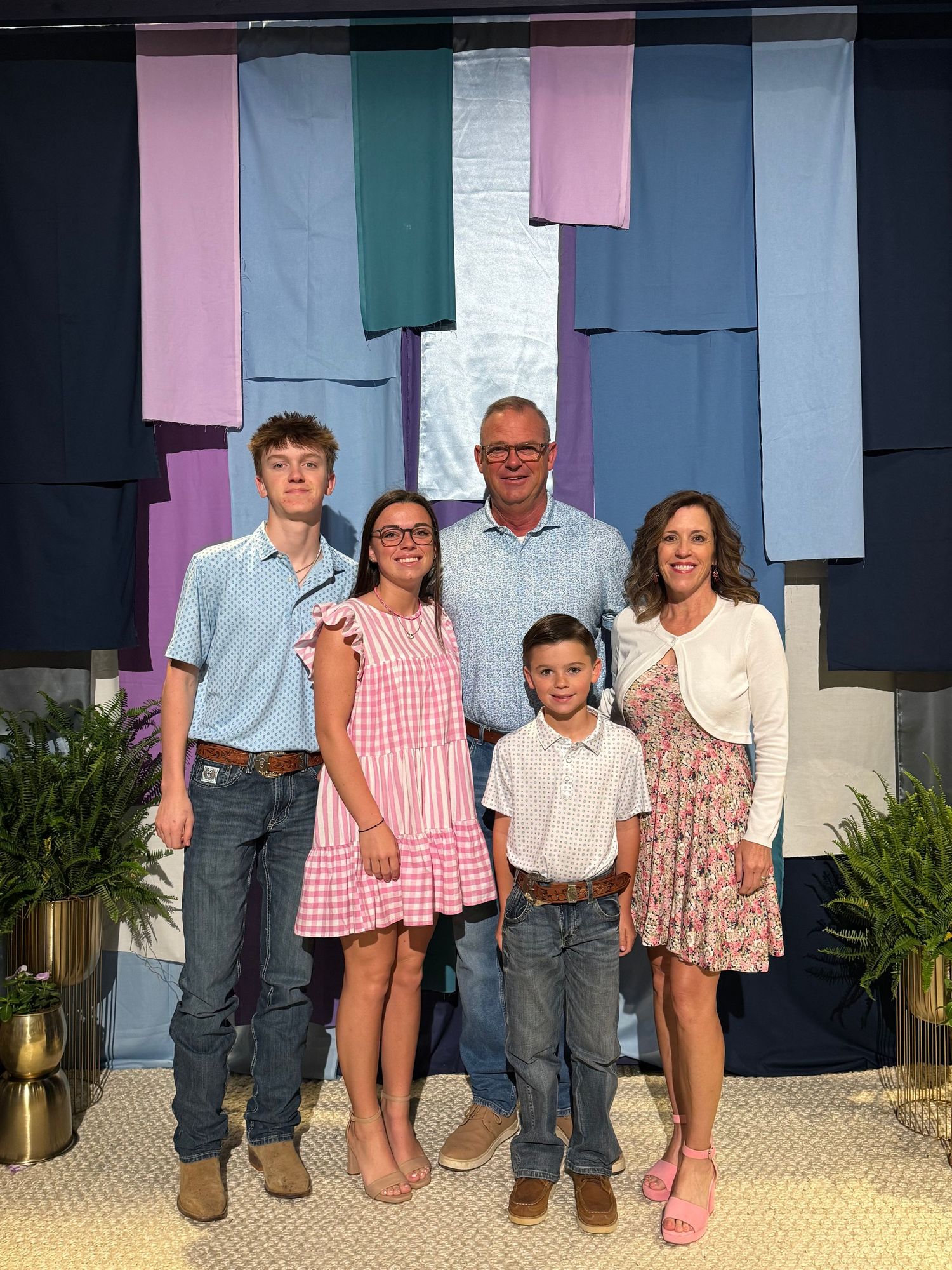 A group of people in casual attire stand together against a blue and pink backdrop with hanging paper decorations.