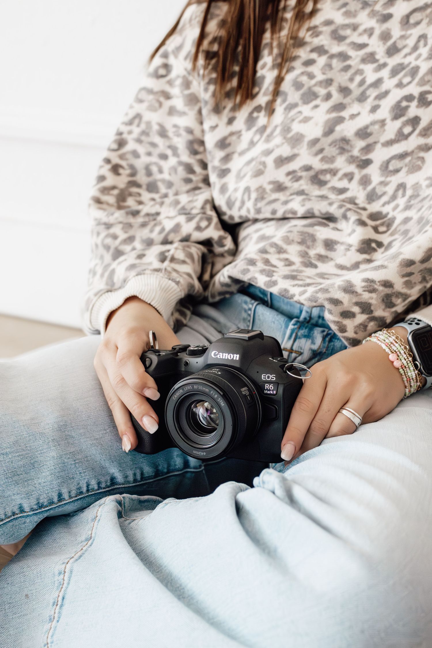 Woman in leopard print sweater and jeans holding a Canon EOS R50 mirrorless camera on her lap.