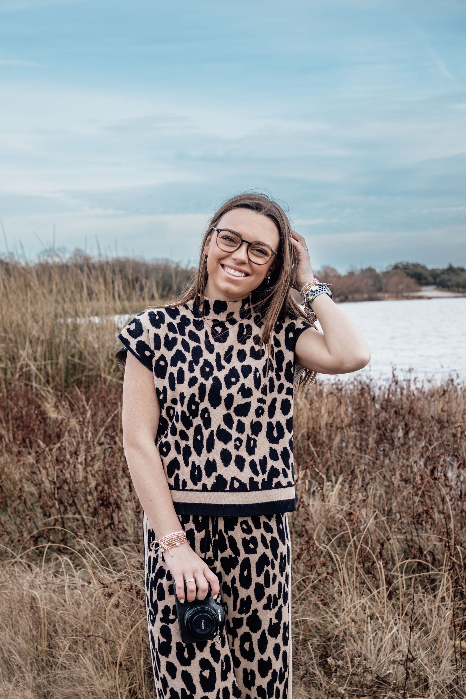 A person in a leopard print dress poses outdoors in a field against a cloudy sky.