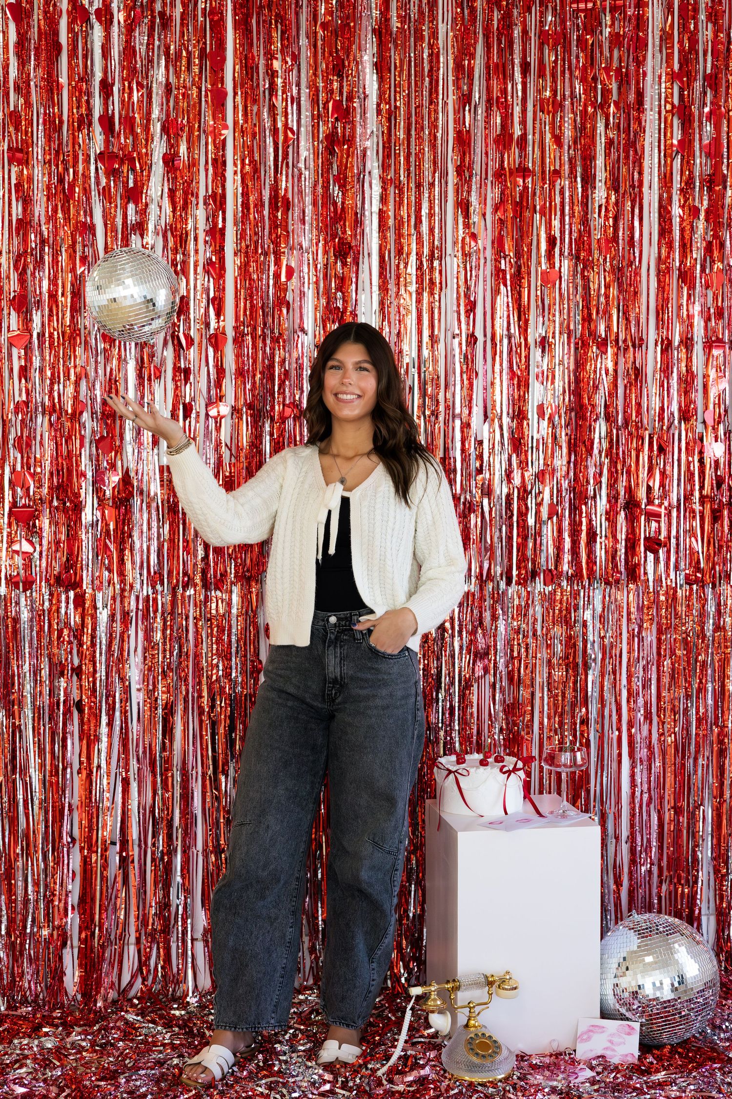 People posing in front of a shimmering red tinsel backdrop with disco balls and white boxes for a festive photo shoot.