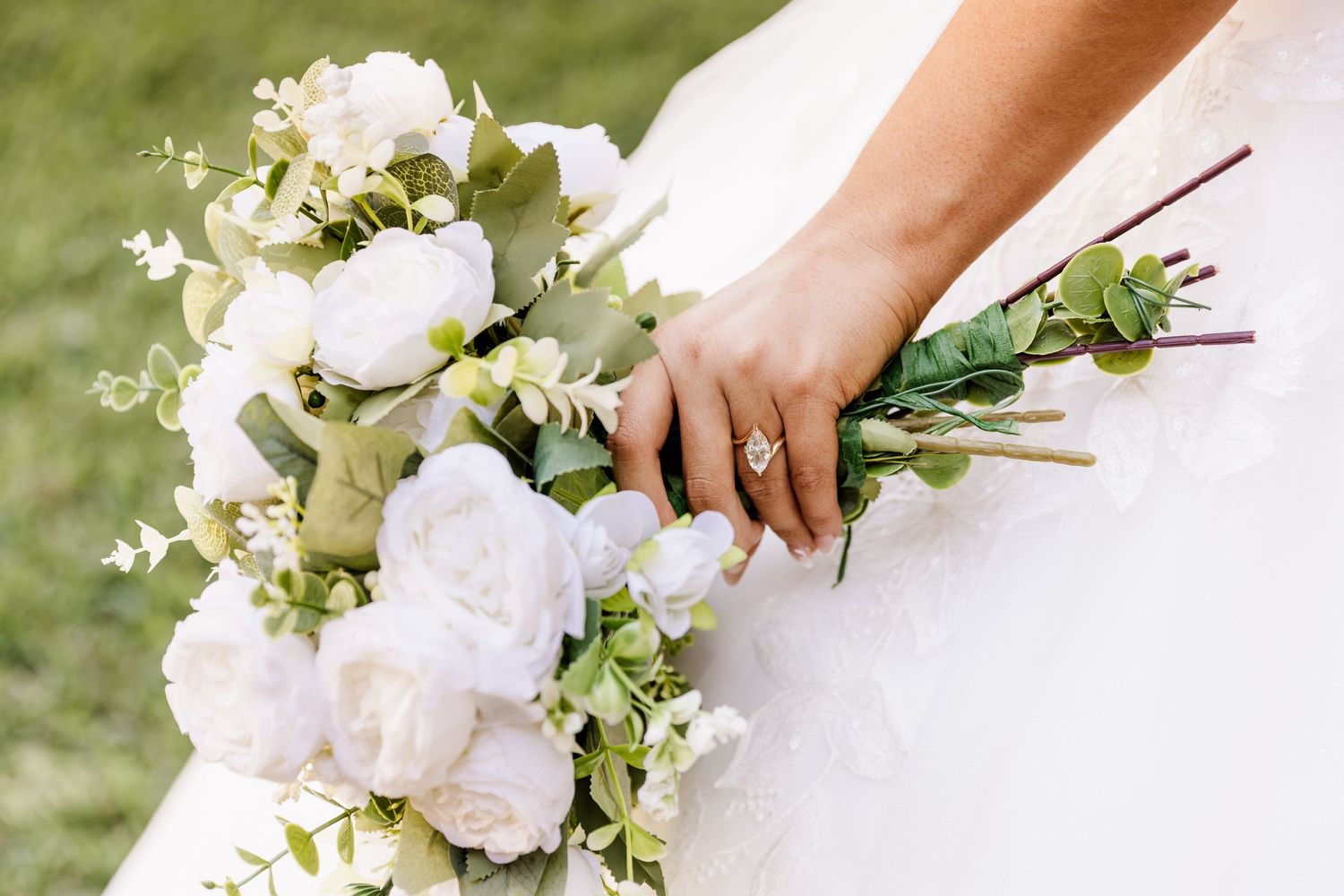 Bride holding a white peony and eucalyptus wedding bouquet, with a diamond ring visible on her hand.