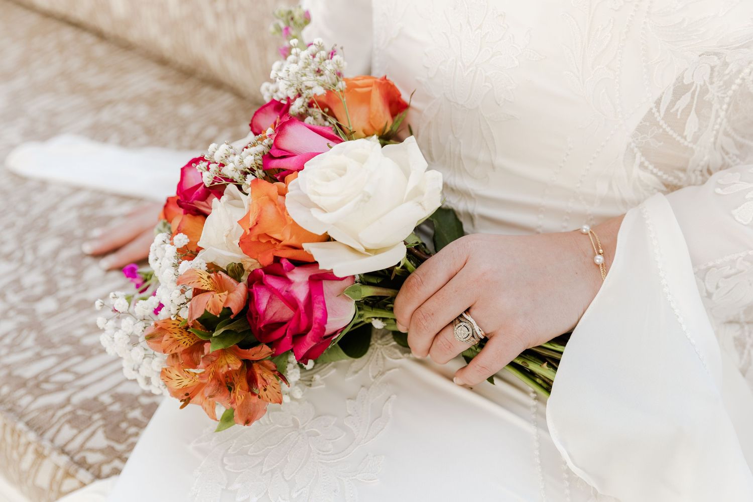 Bride holding a vibrant wedding bouquet with white, pink, and orange roses, wearing a diamond ring on her finger.