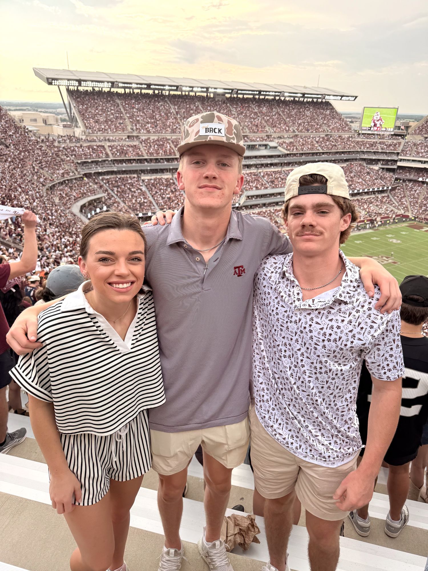 Friends posing together at a crowded football stadium on a sunny game day.