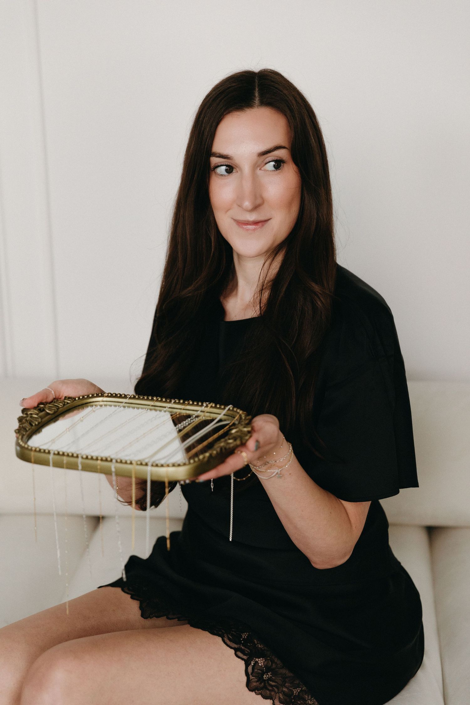Woman in black dress holding ornate gold decorative tray while sitting on white couch.
