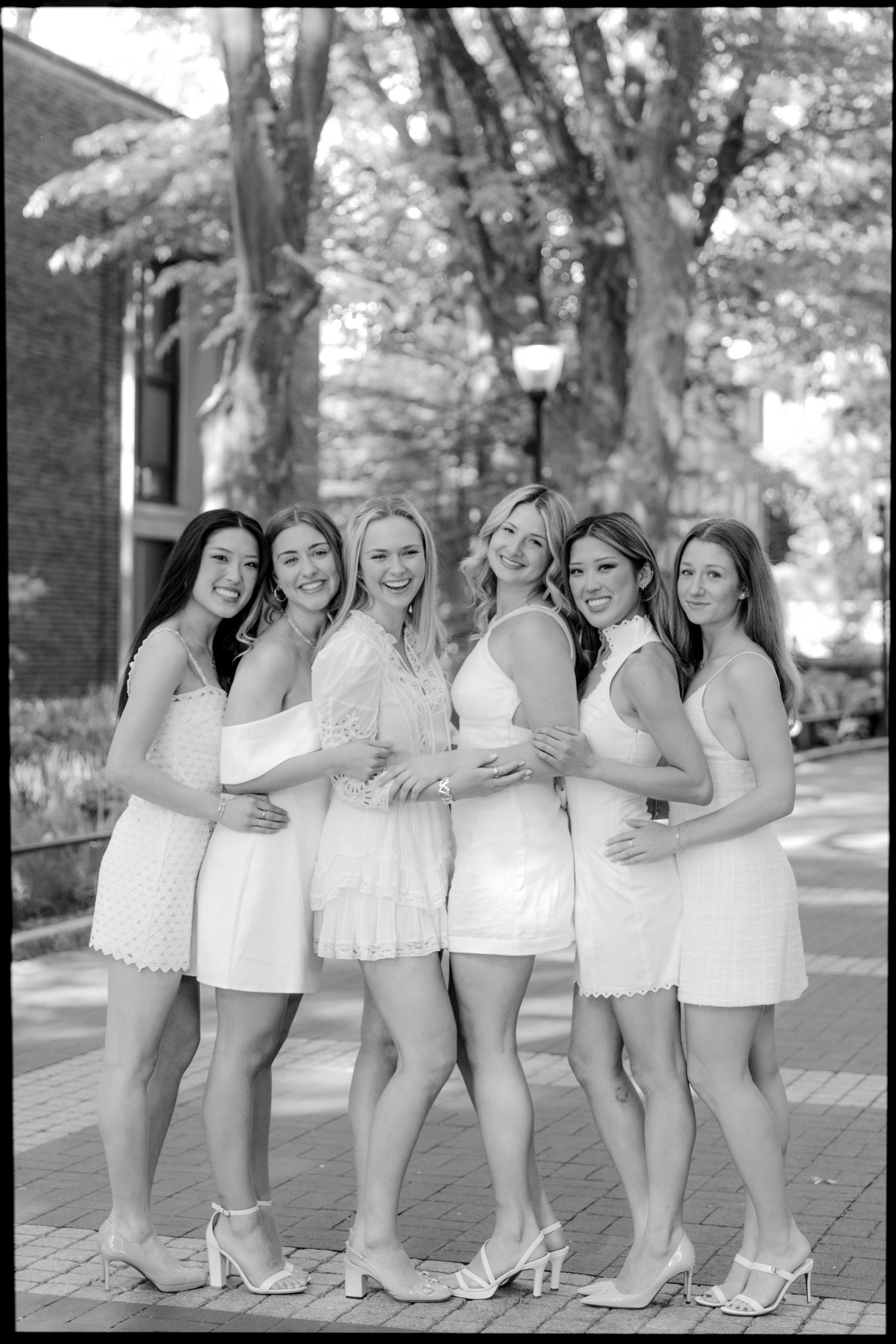 Black and white photo of graduates in white dresses posing together on campus grounds.