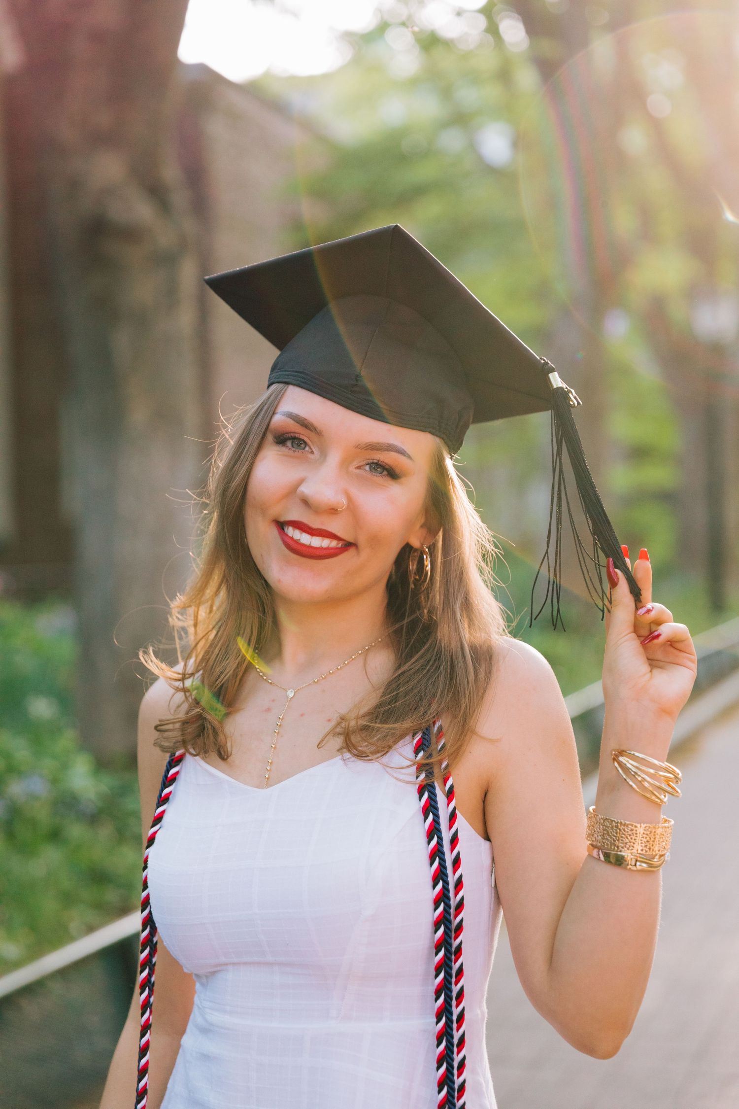 Graduate wearing cap and white dress smiles while posing outdoors.