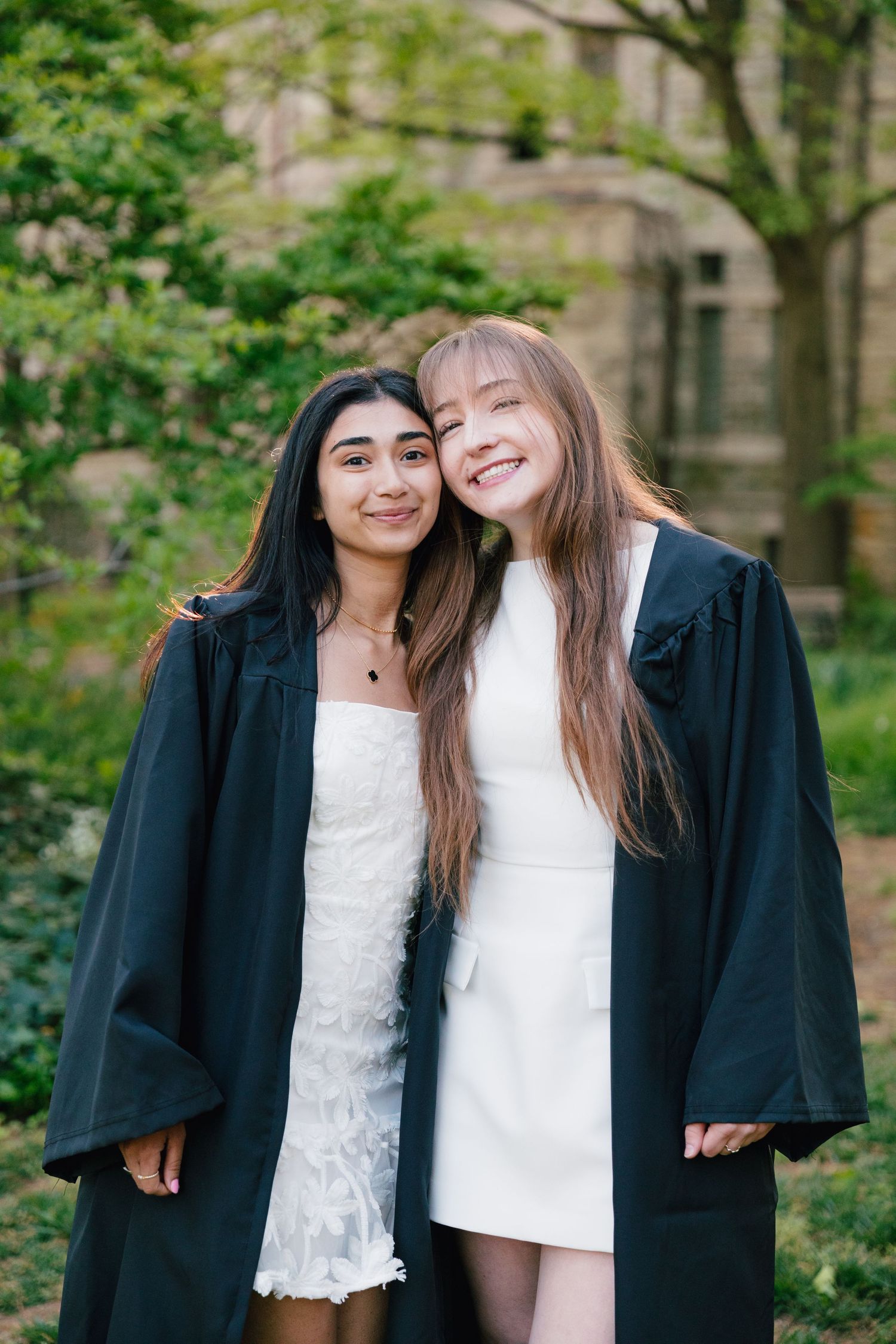 Two graduates in black gowns share joyful moments together on a spring day.
