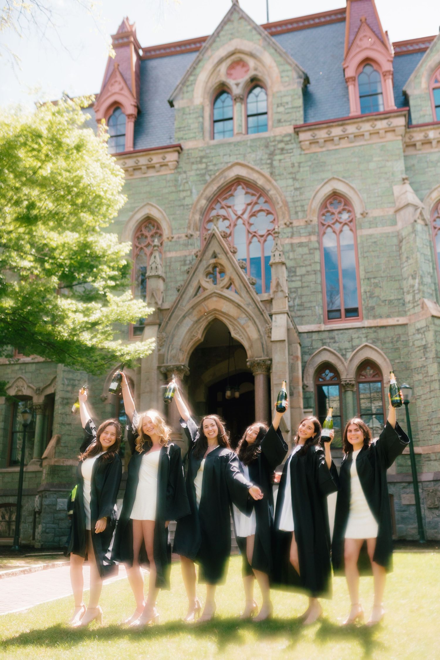 Graduates celebrate in front of a Victorian Gothic university building with ornate architecture.
