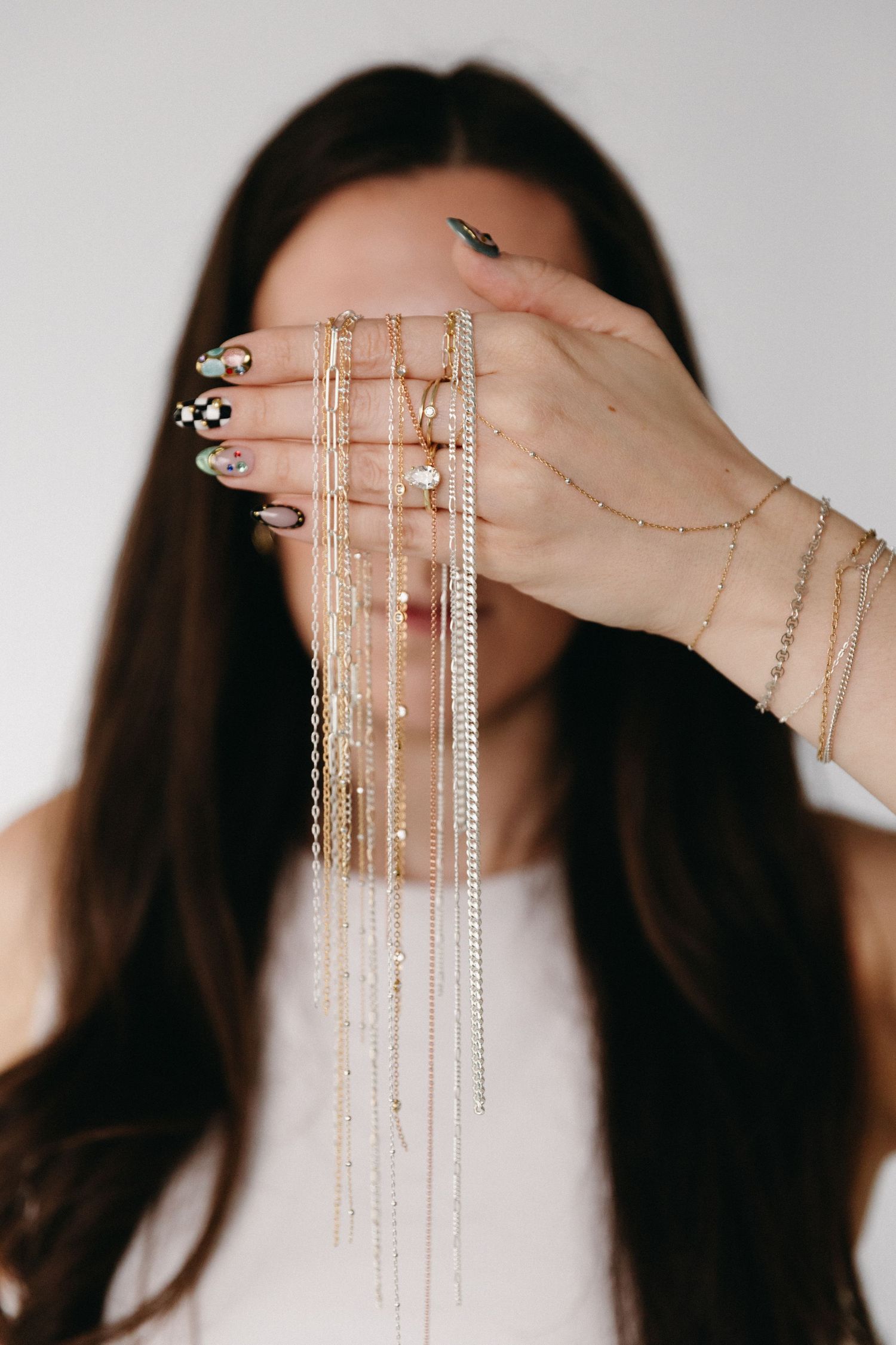 Woman holding multiple gold chain necklaces in front of her face, showcasing layered jewelry and decorated nails.