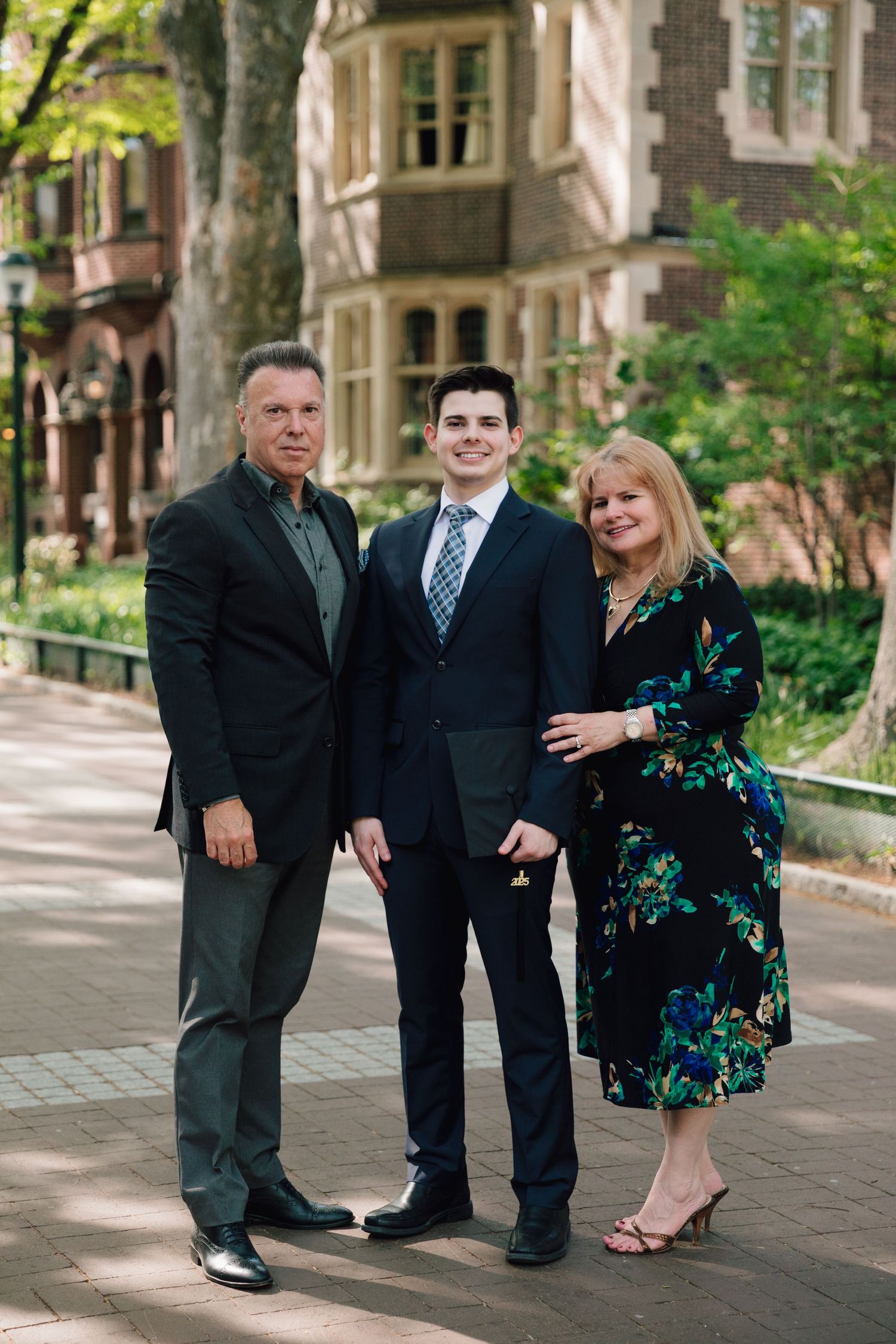 Family poses together on tree-lined university walkway during graduation day.