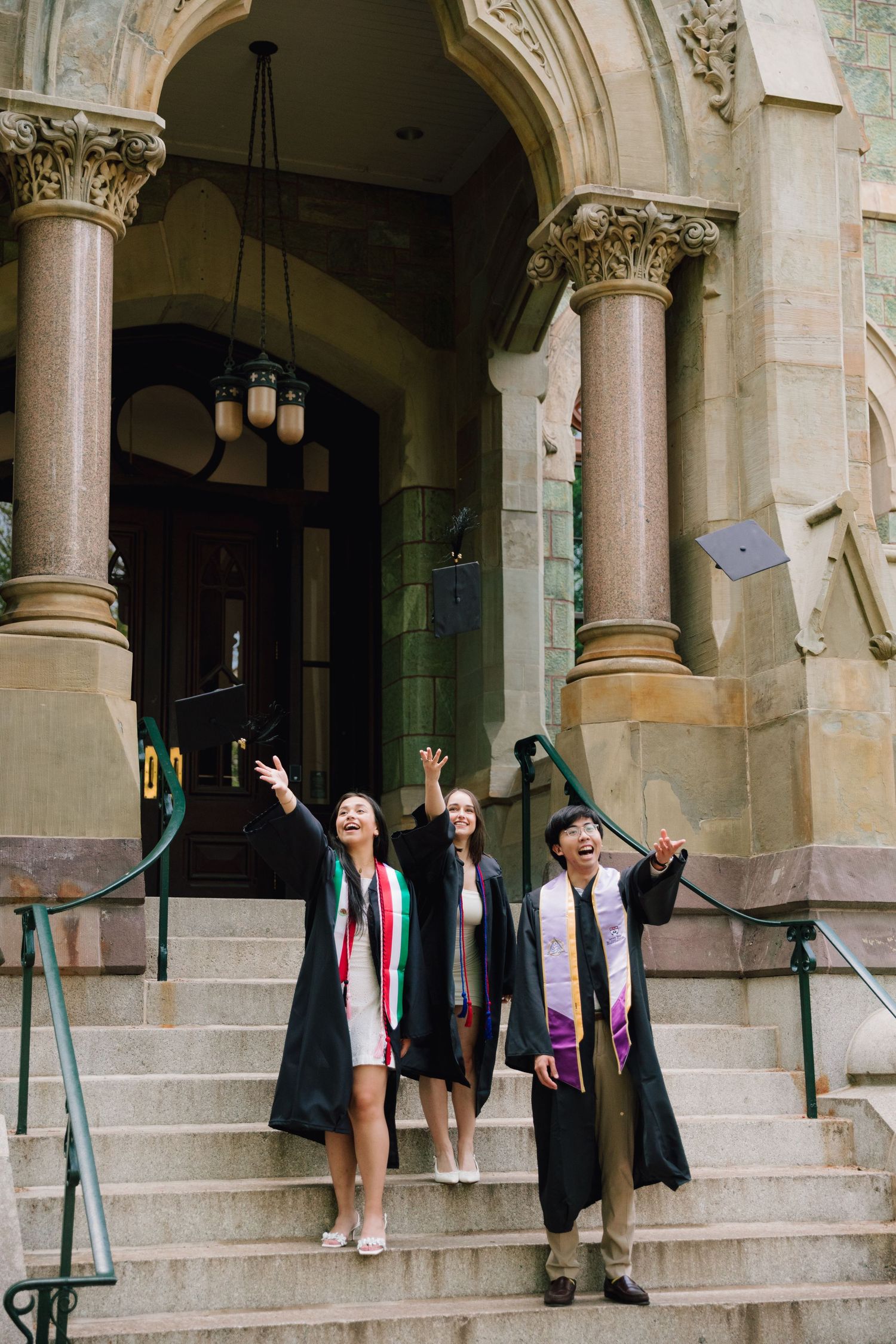Graduates toss caps in celebration on stone steps of historic building.