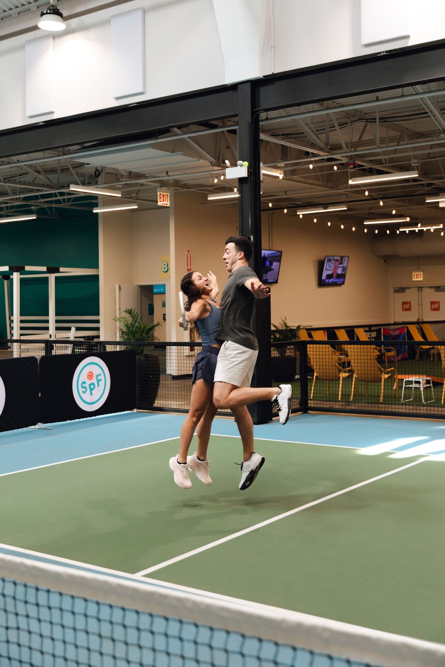 Two players joyfully jump and celebrate on an indoor pickleball court at SPF facility.