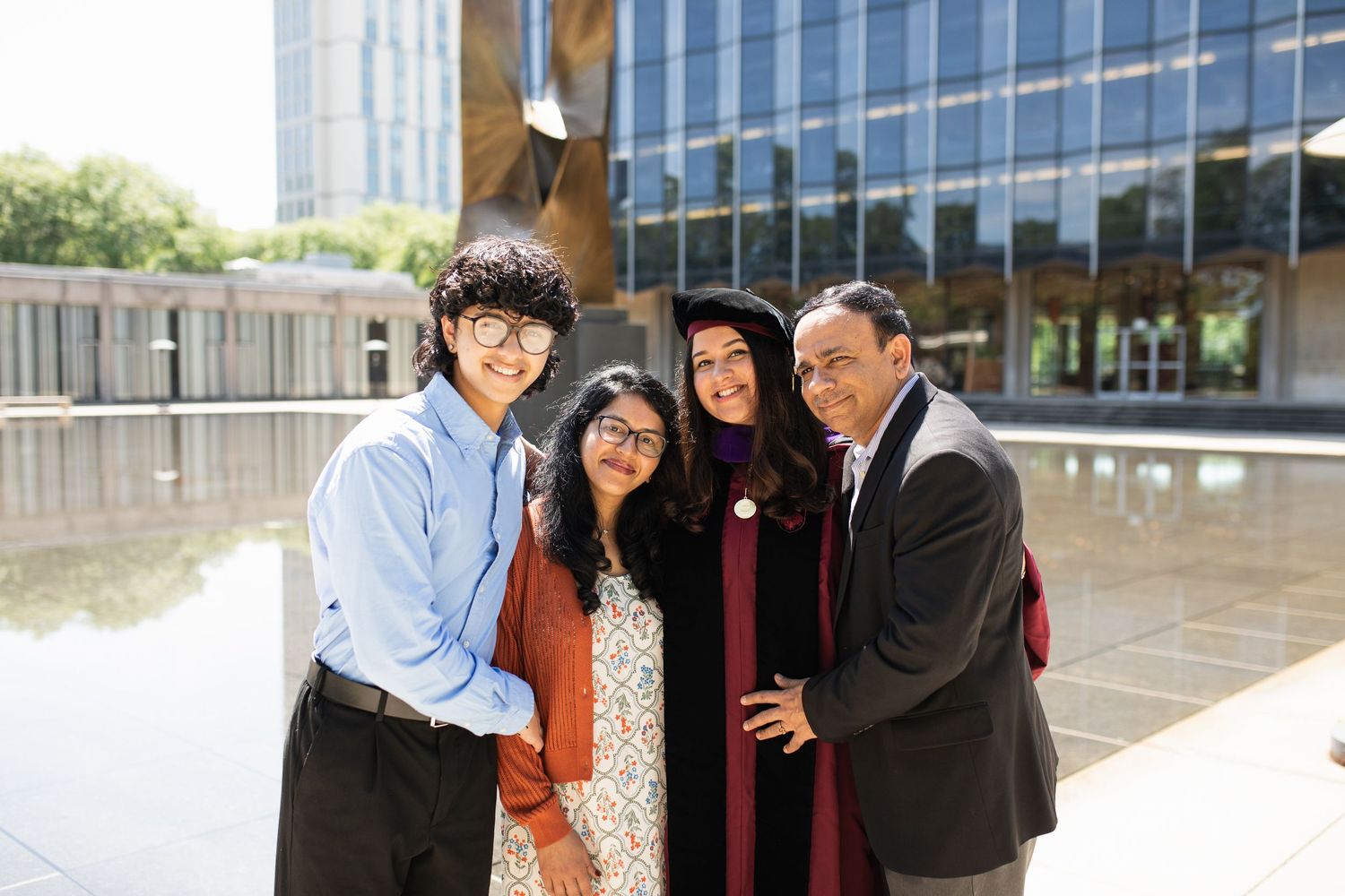 Group photo of graduates in academic regalia celebrating together outside modern office building.