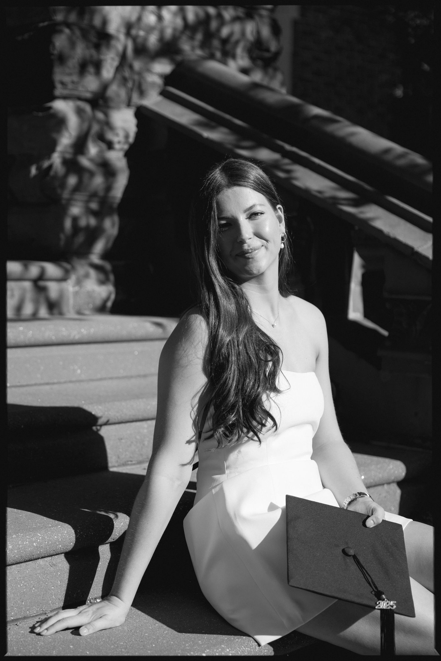 Black and white graduation portrait on stone steps in dramatic lighting.