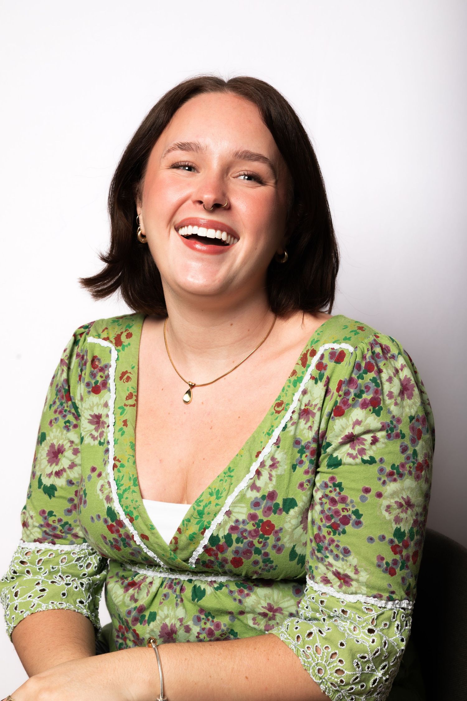 A young woman in a green floral dress laughs joyfully against a white background.