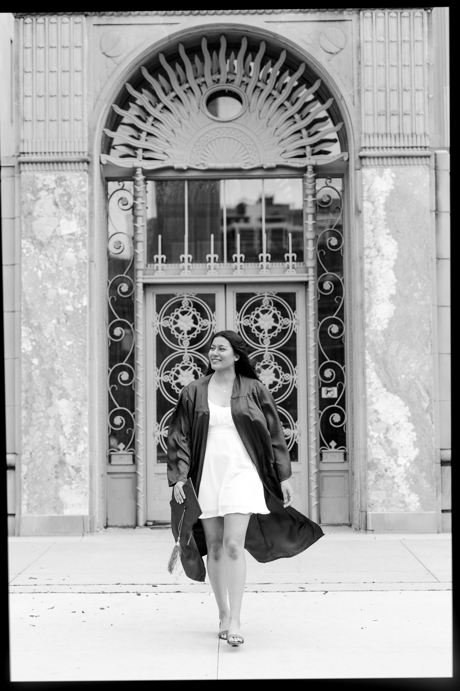 Graduate in black coat poses in front of ornate vintage doorway with sunburst architectural detail.