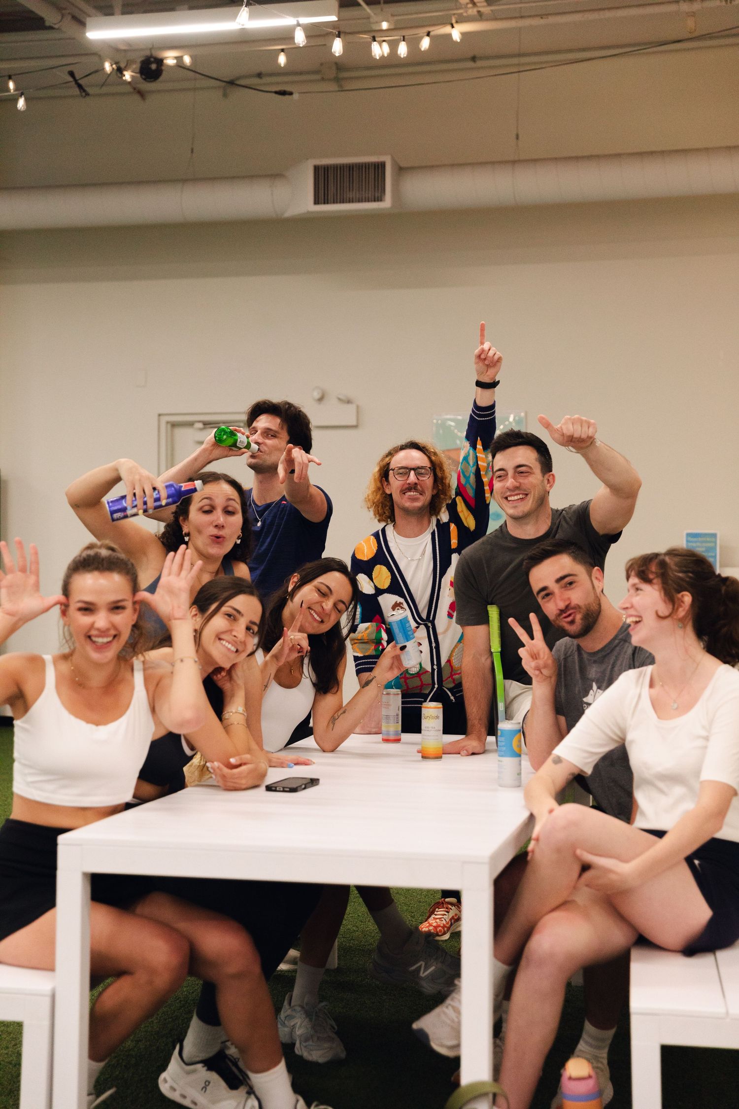 Group of young adults in athletic wear posing and smiling around a white table in a bright indoor space.