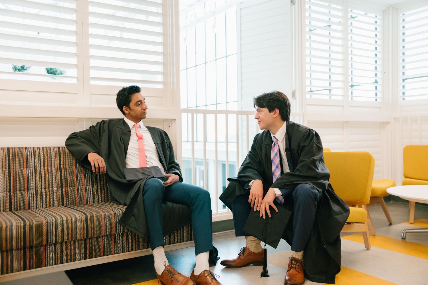 Casual indoor graduation portraits on striped seating with window lighting.