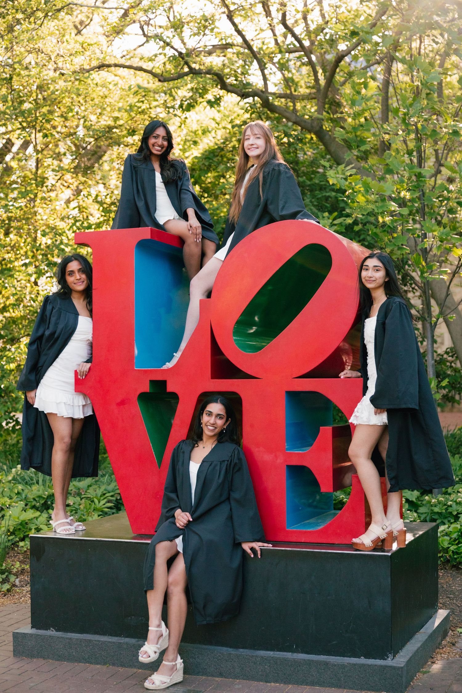Graduation photos taken around large red LOVE sculpture on university campus.