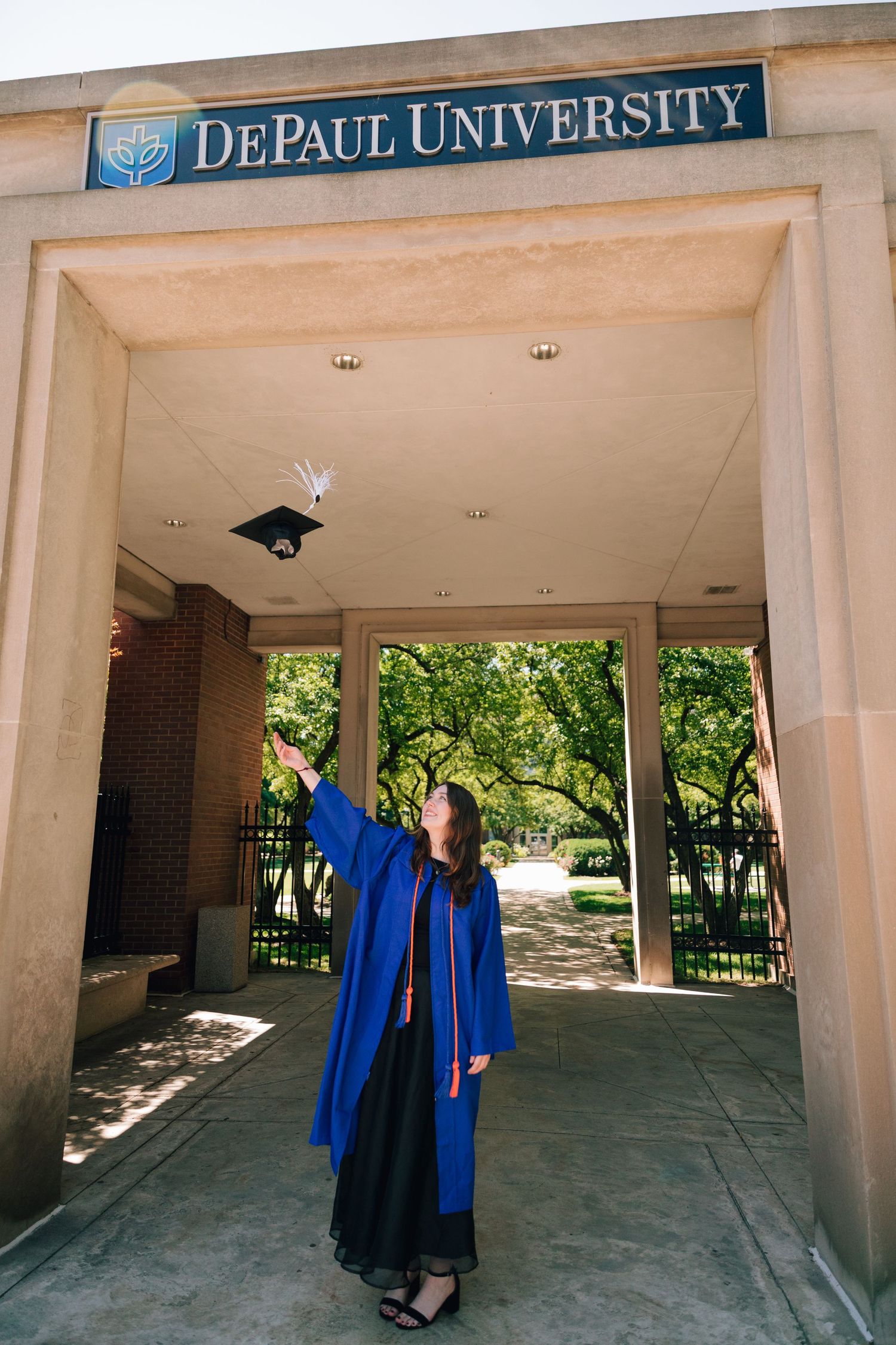 Graduate tosses cap beneath DePaul University entrance arch in celebratory pose.