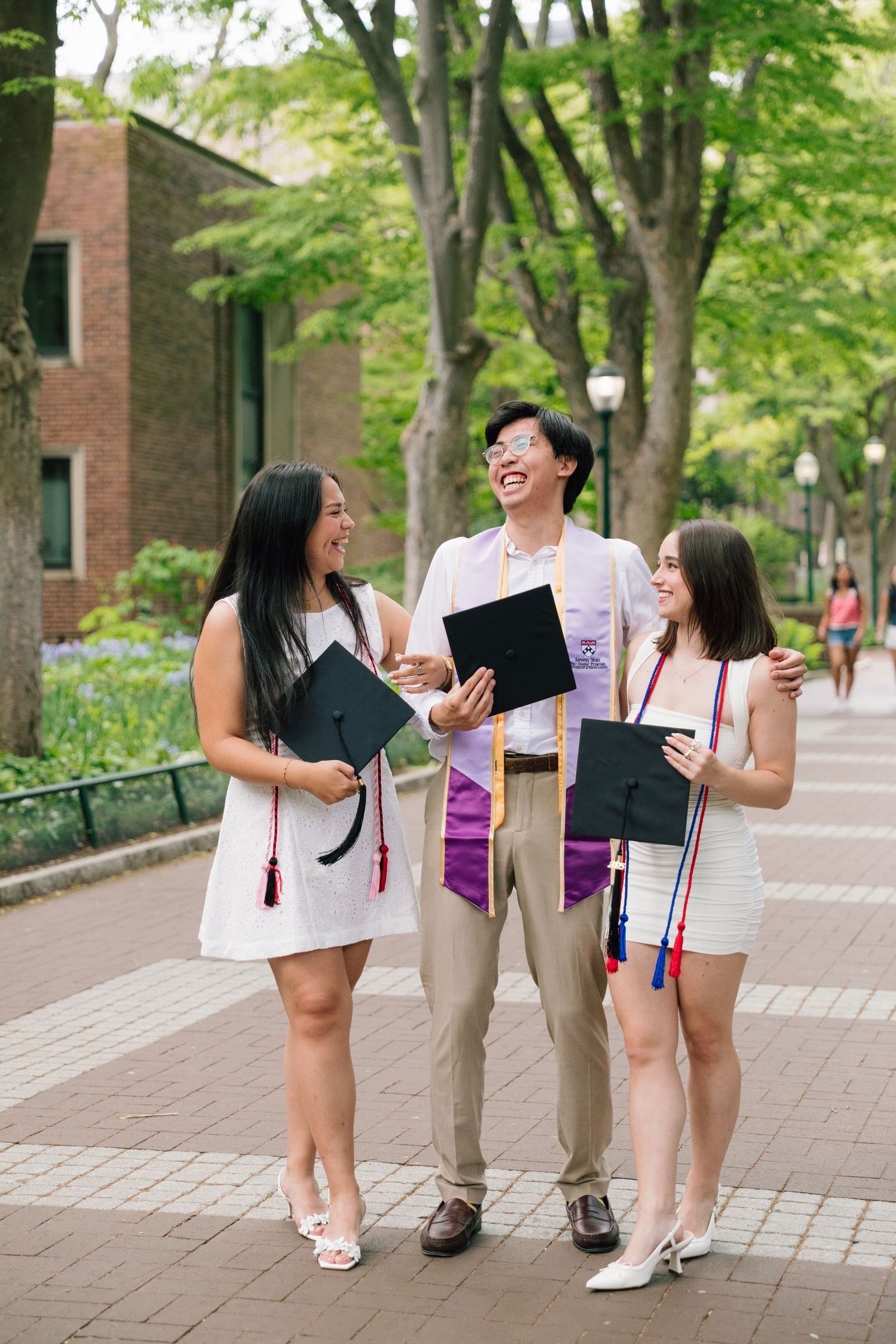 Students laughing while reviewing documents together on a tree-lined university walkway.