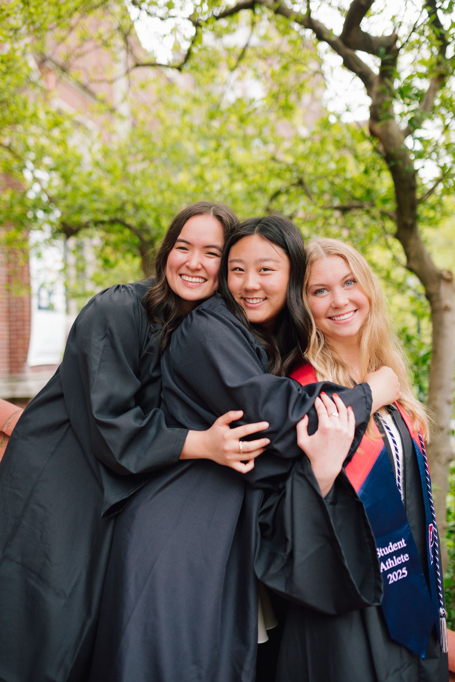 Graduates in black robes share joyful embrace during commencement celebrations.