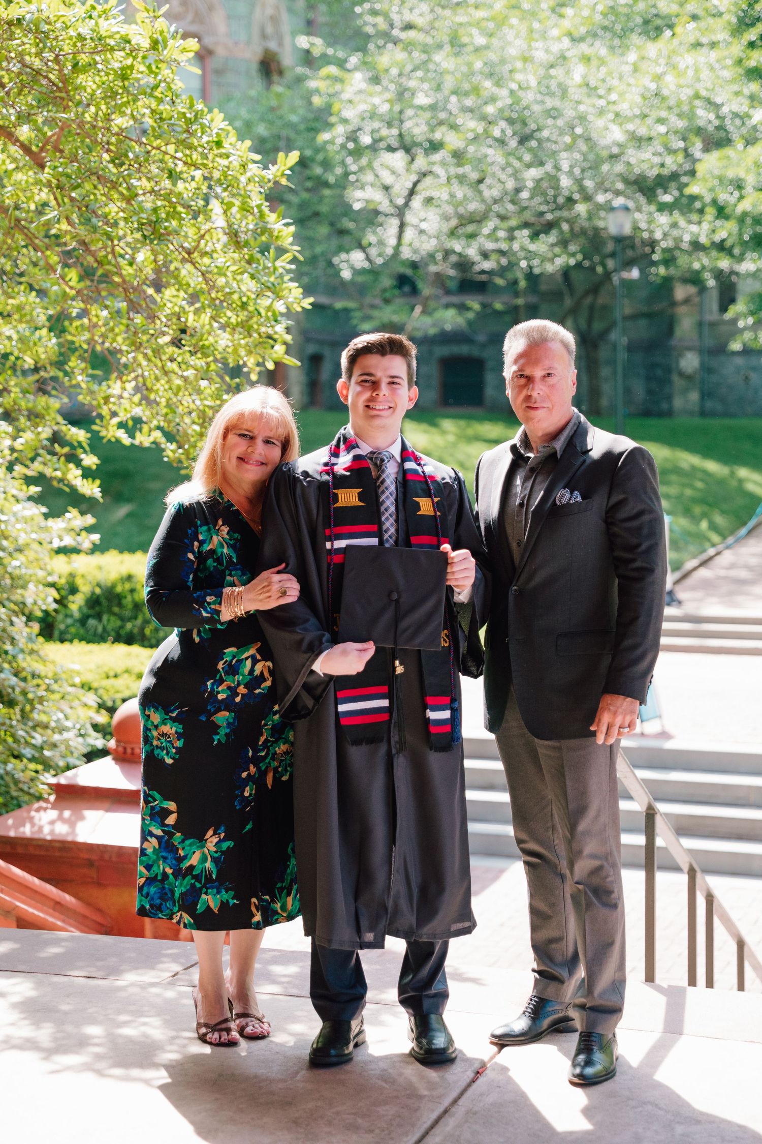 Family graduation portrait taken on sunny stone steps with ornate architecture.