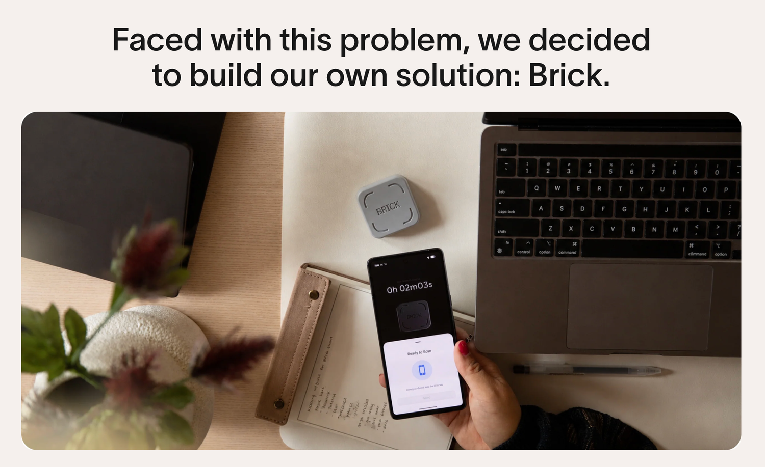 Person holding a phone displaying Brick app, next to a laptop and small device on a desk.
