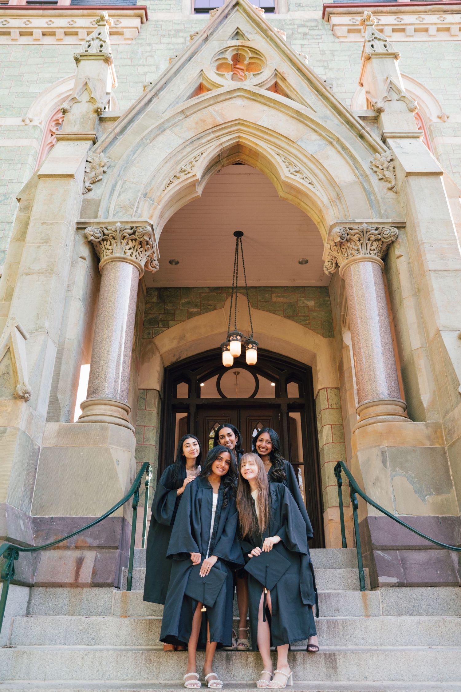 Graduates pose in front of ornate gothic architecture with decorative stone archways.