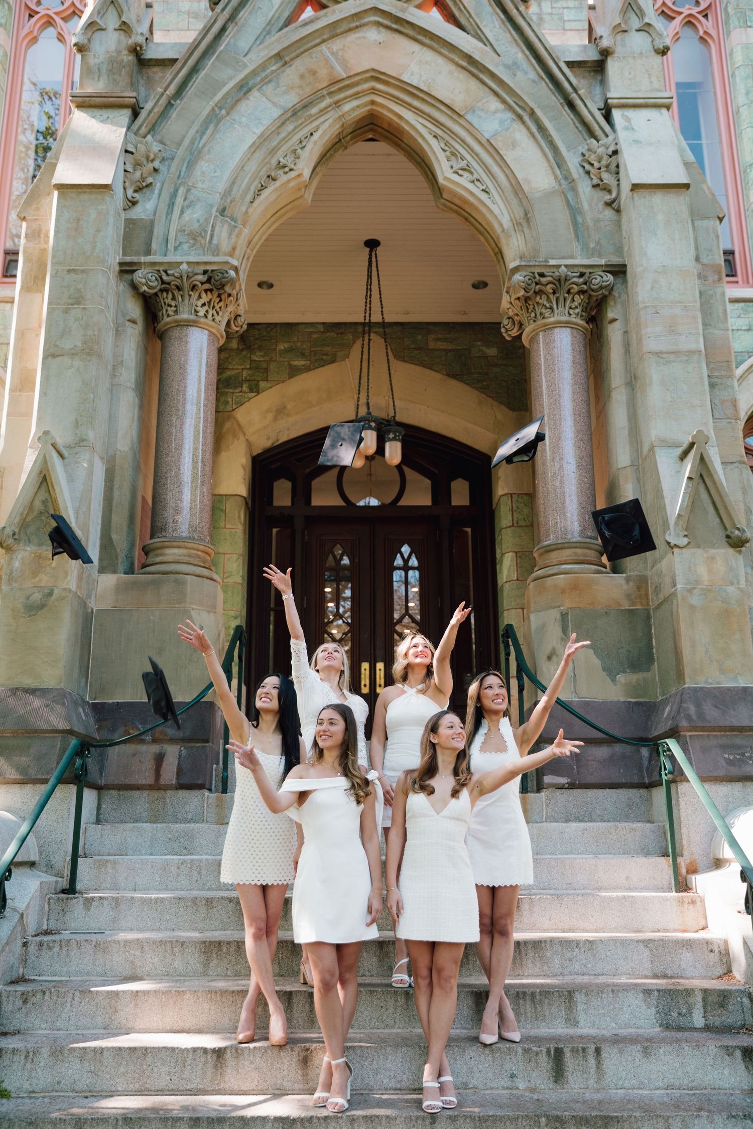 Graduates throw caps in celebration on grand stone steps of gothic university entrance.