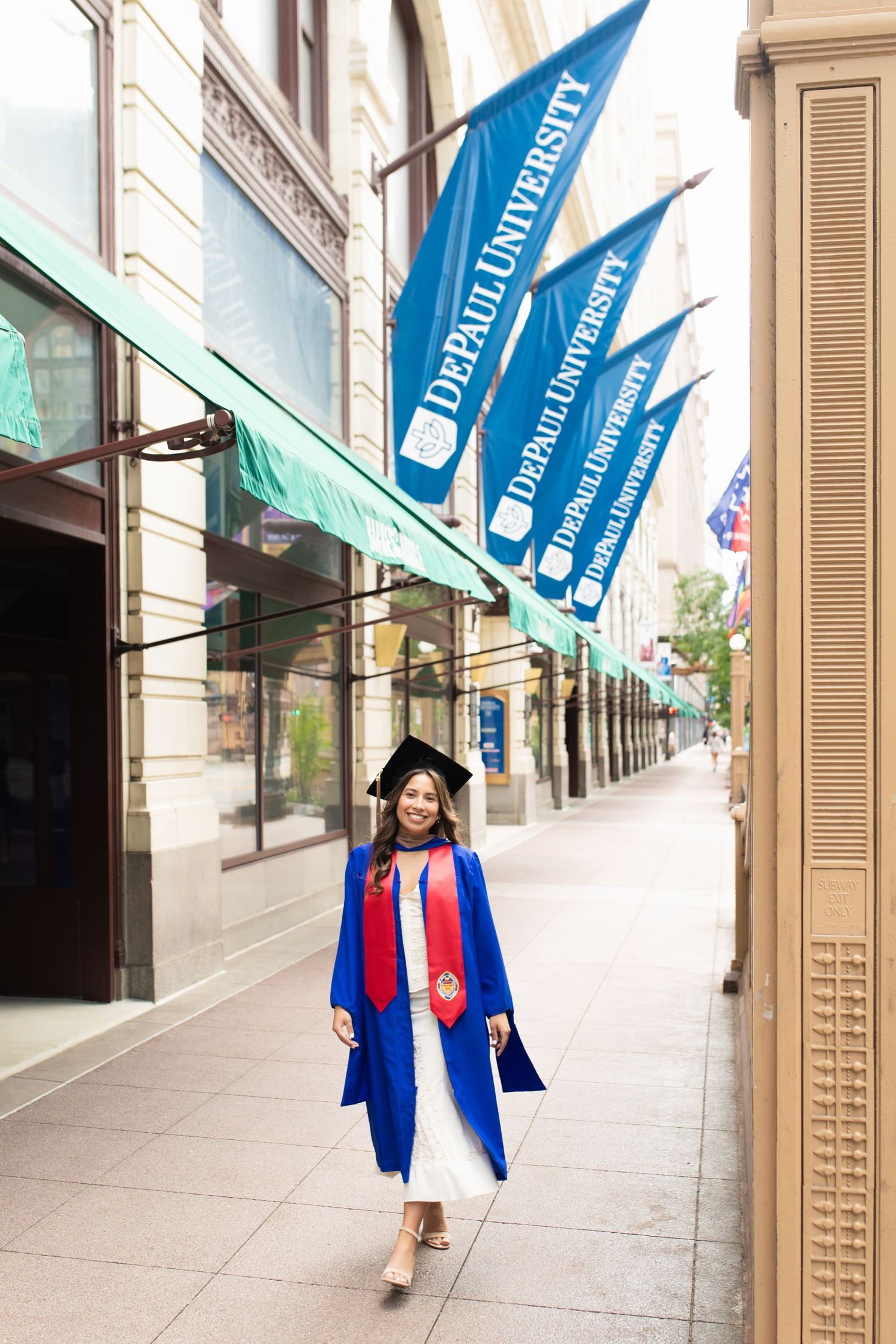 DePaul University banners line a city sidewalk with graduate walking beneath.