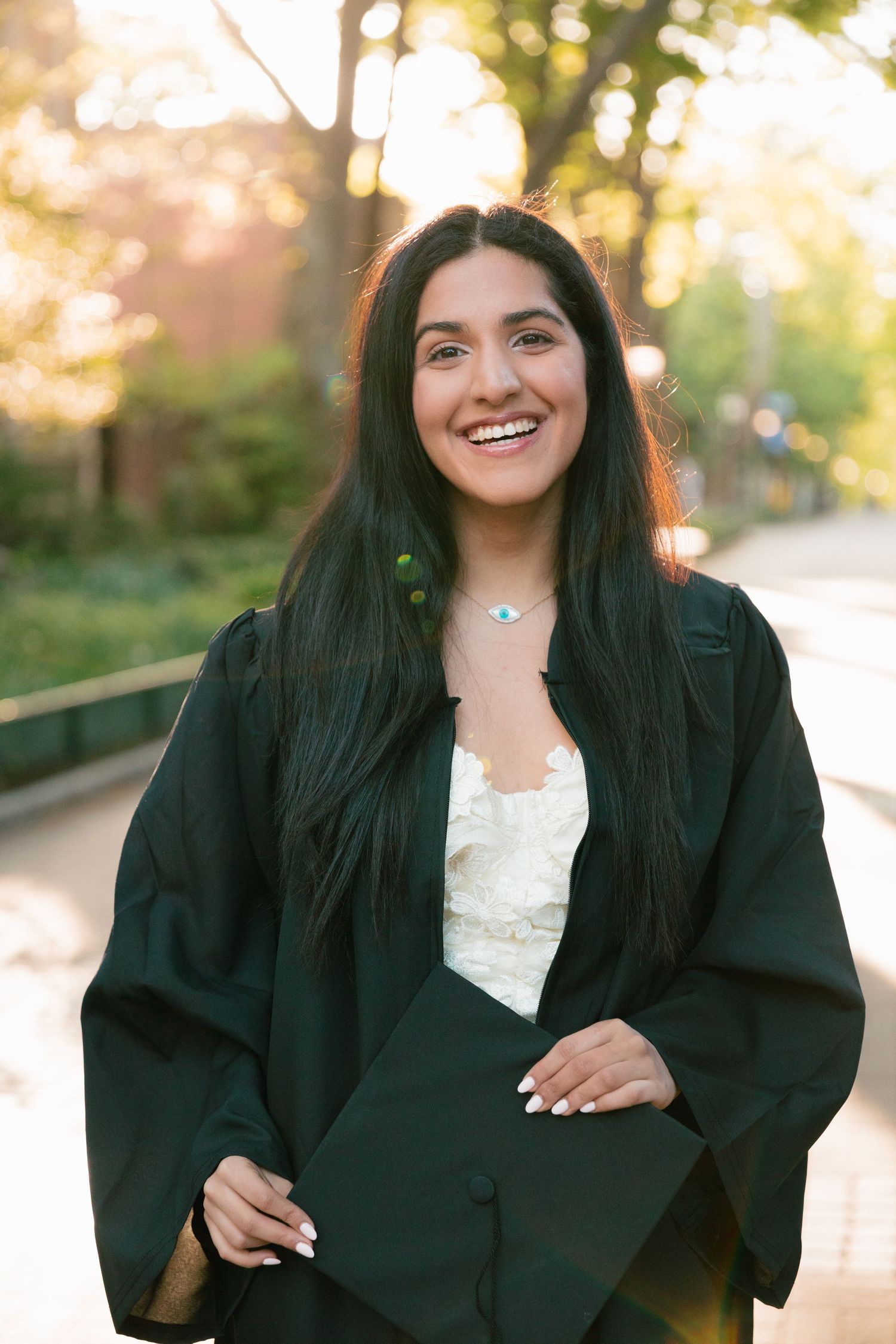 Graduate in black academic regalia poses outdoors during golden hour.