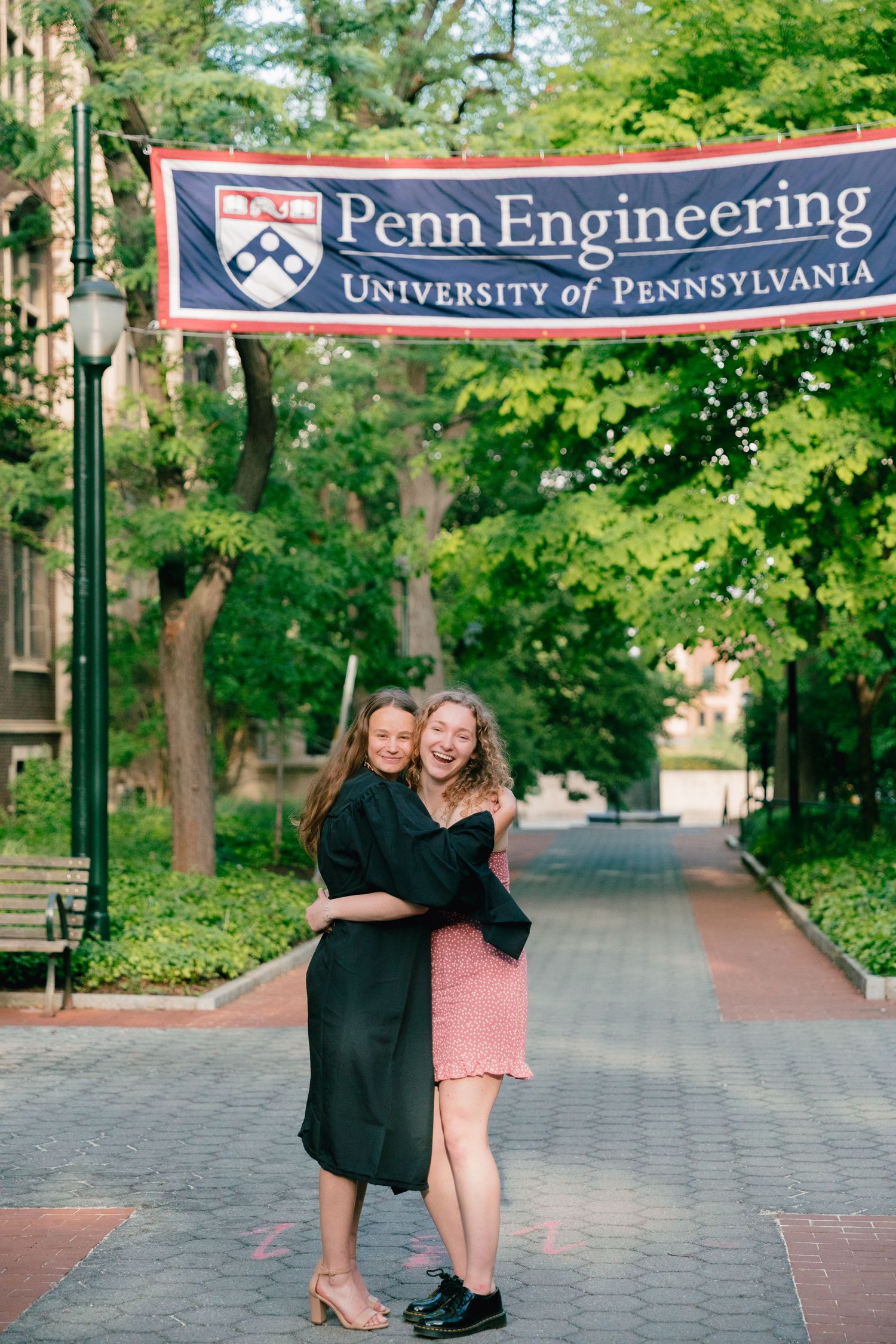 Students pose for graduation photos in front of Penn Engineering banners on campus walkway.