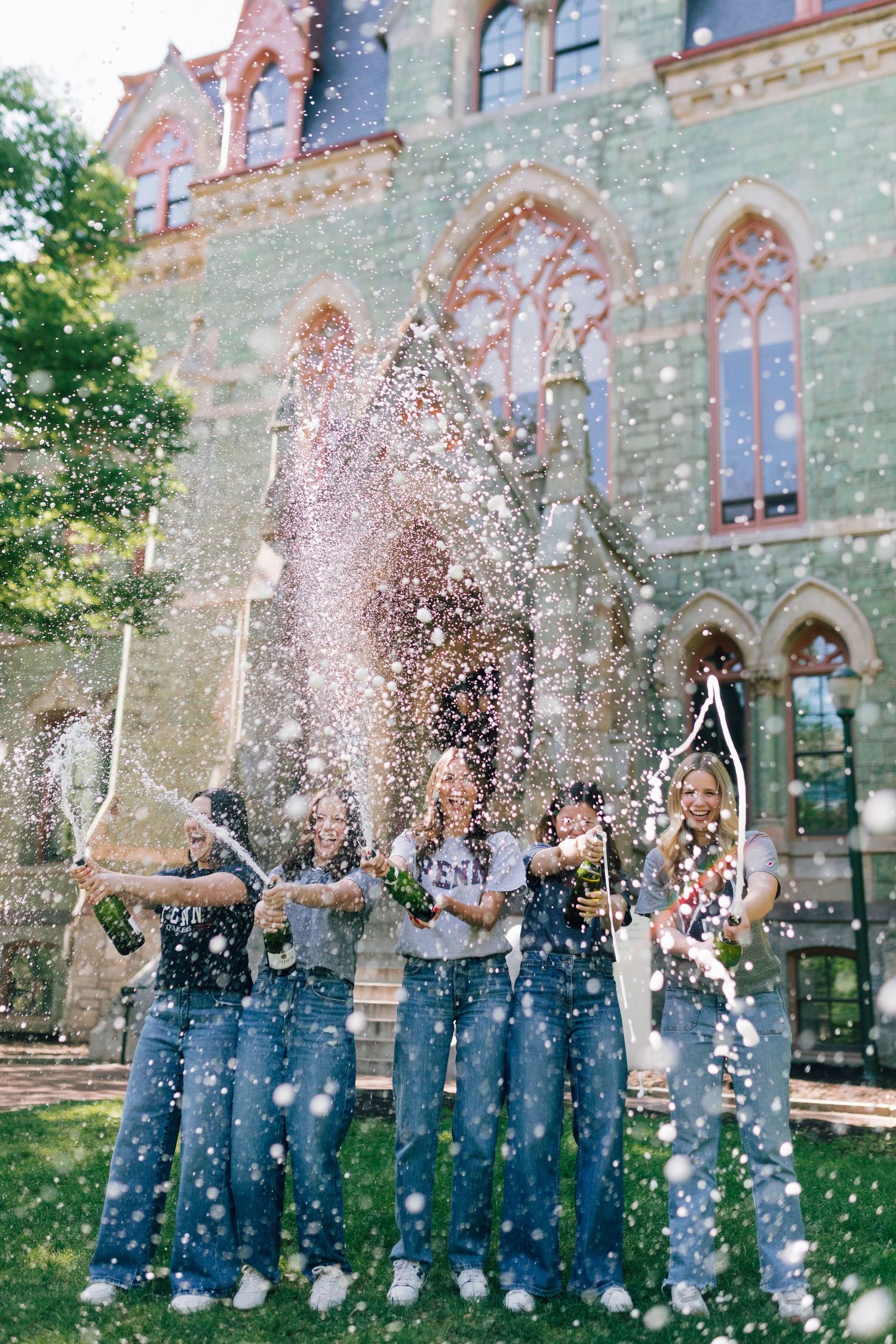Group celebrates with champagne spray in front of historic stone building.