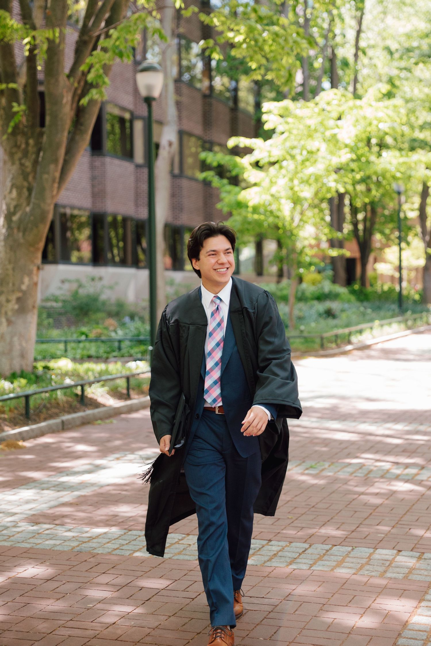 Graduate walks joyfully along brick pathway during graduation photo session.