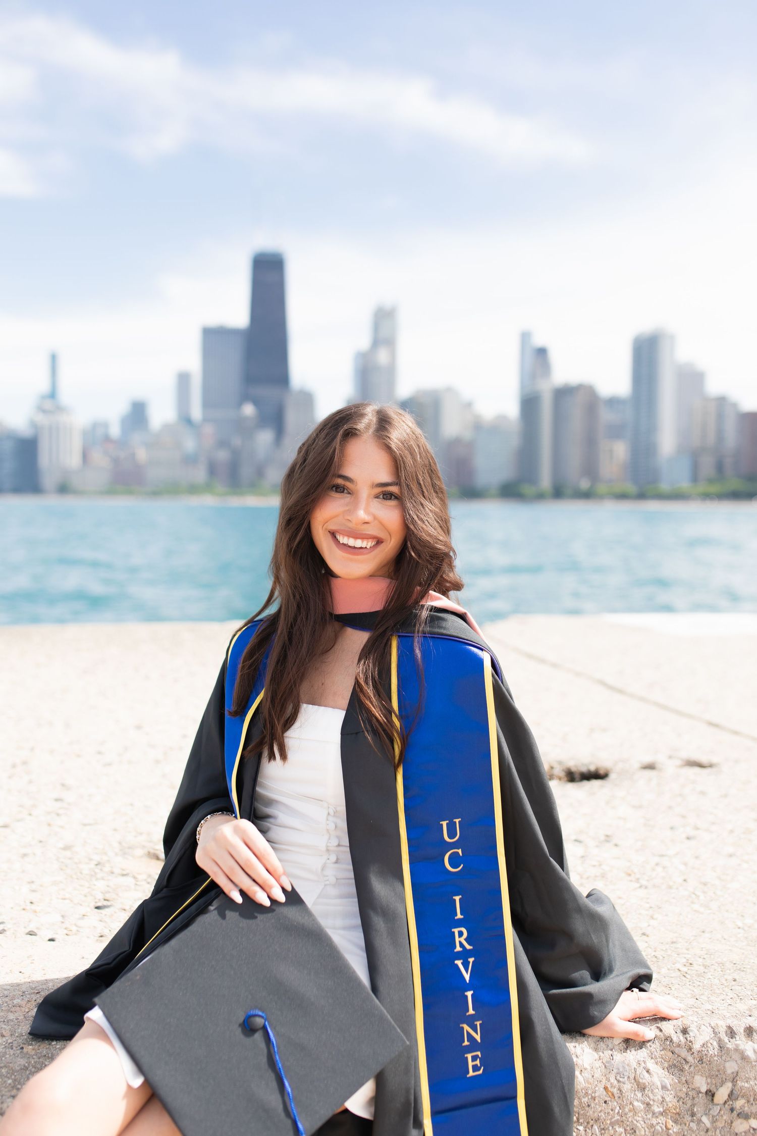 Graduate in blue stole poses near Lake Michigan with Chicago skyline backdrop.