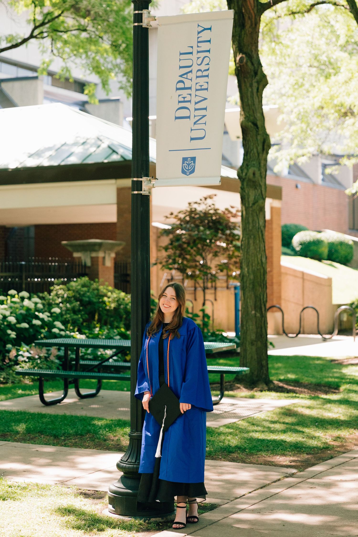 Graduate poses beneath DePaul University banner in blue commencement regalia.