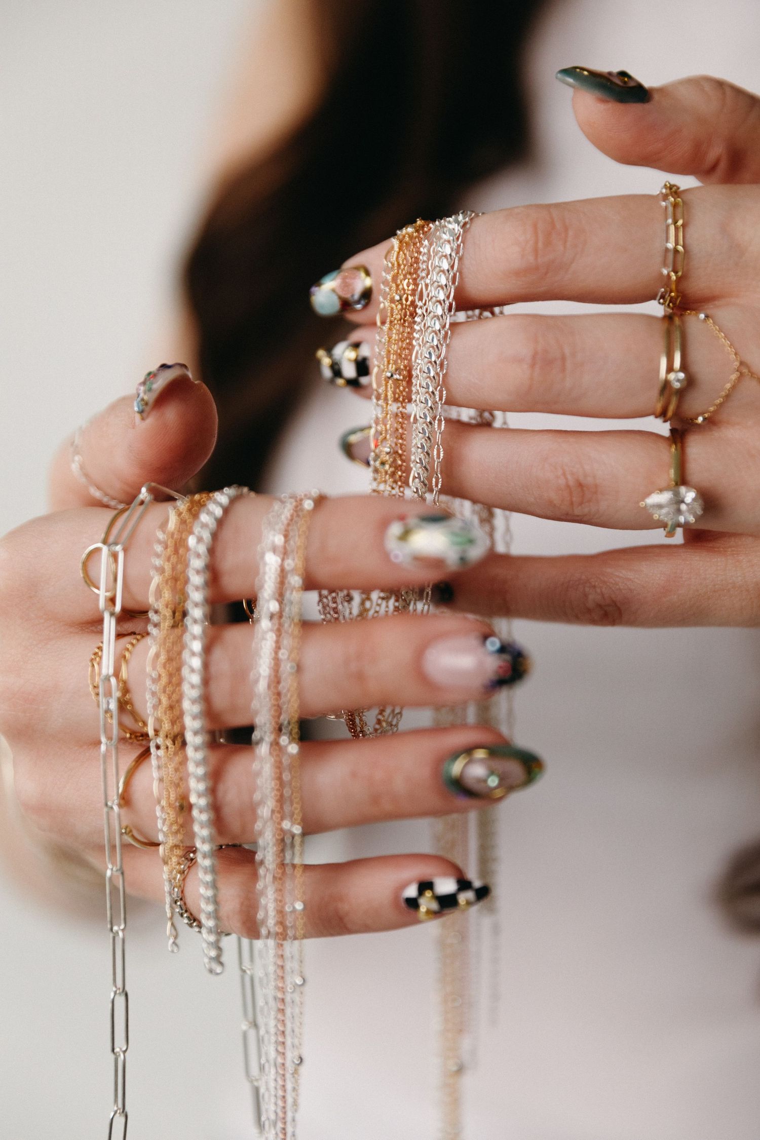 Close-up of hands adorned with multiple gold and silver rings, layered chains, and decorative nail art.